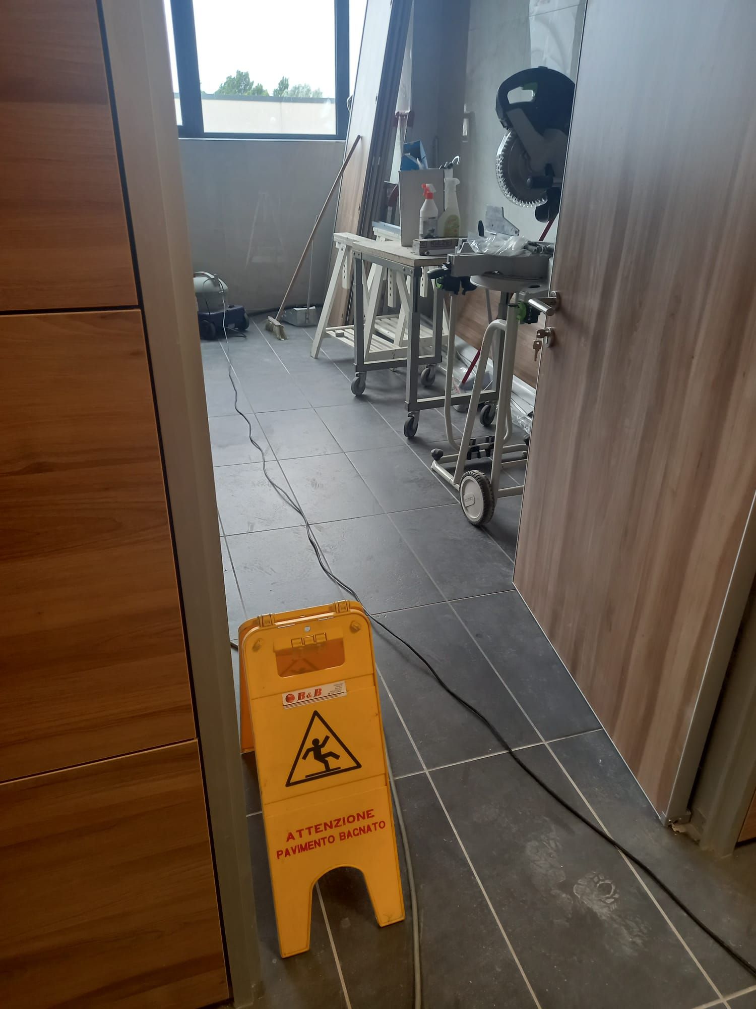 Cartello giallo per pavimento bagnato in uno stretto corridoio d'ufficio con cavi e apparecchiature nelle vicinanze