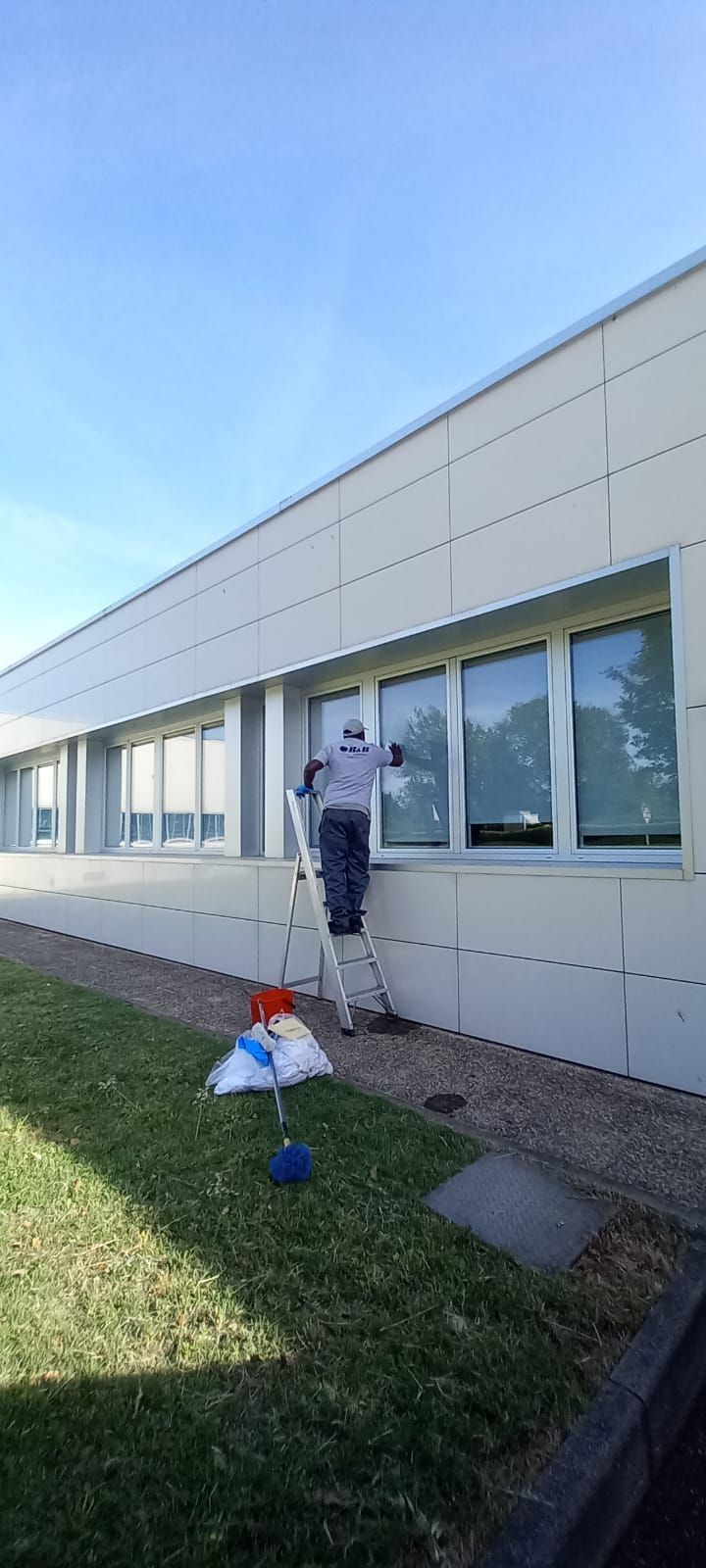 Una persona dipinge la parete esterna di un edificio bianco accanto a un prato e alle finestre.