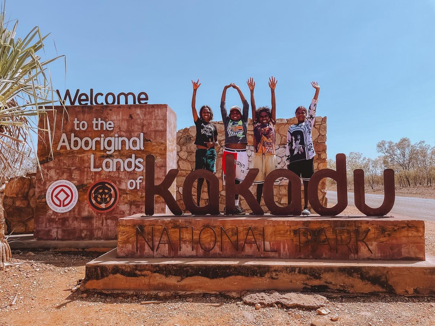 A group of children are standing in front of a sign that says welcome to the aboriginal lands of kakadu national park.