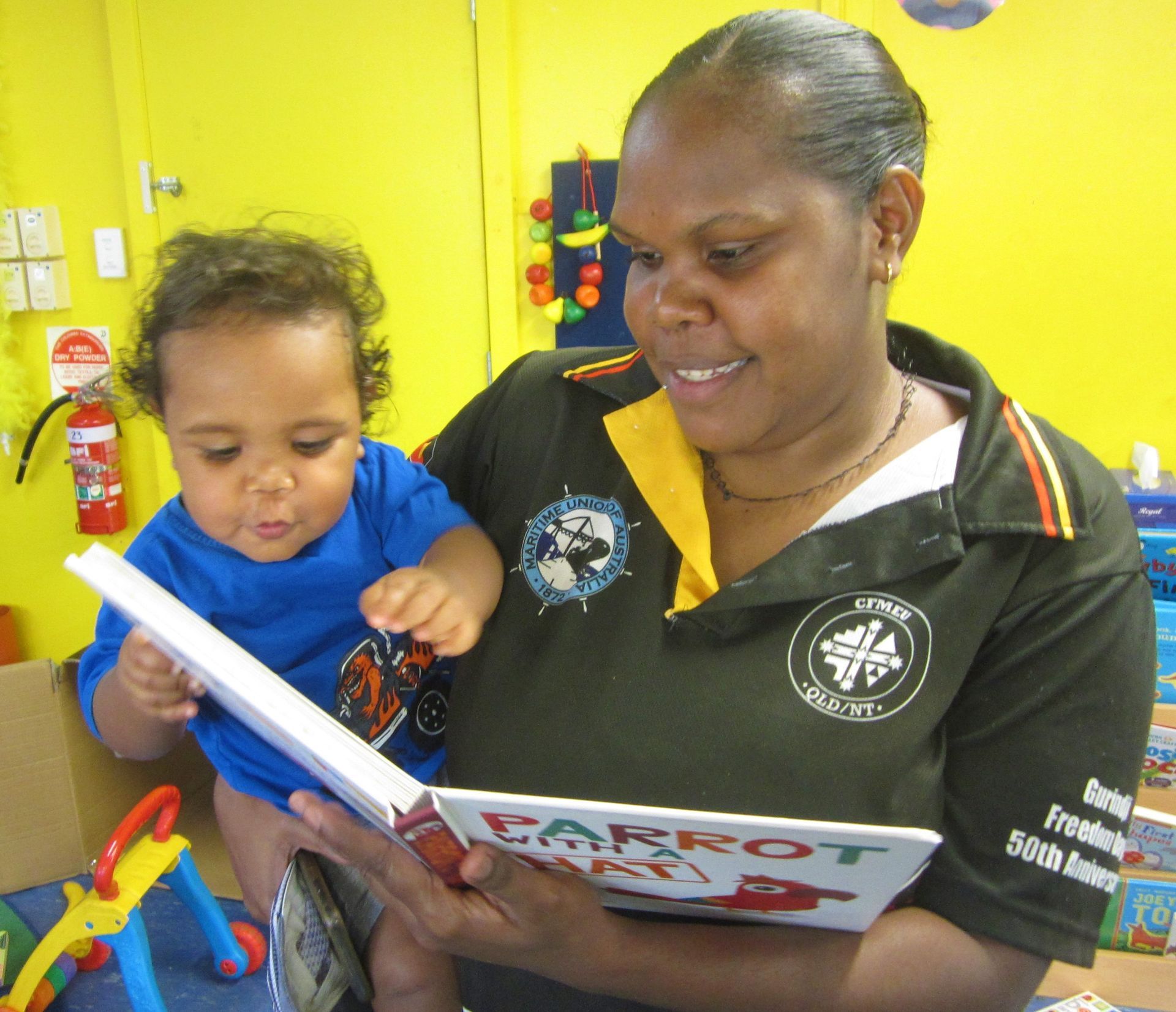 A woman is reading a book to a baby who is holding her