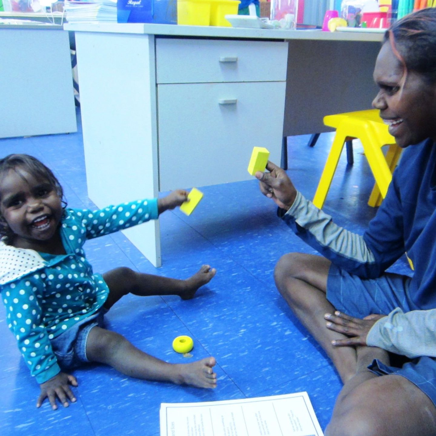 A little girl sitting on the floor with a man holding a piece of paper that says ' a ' on it