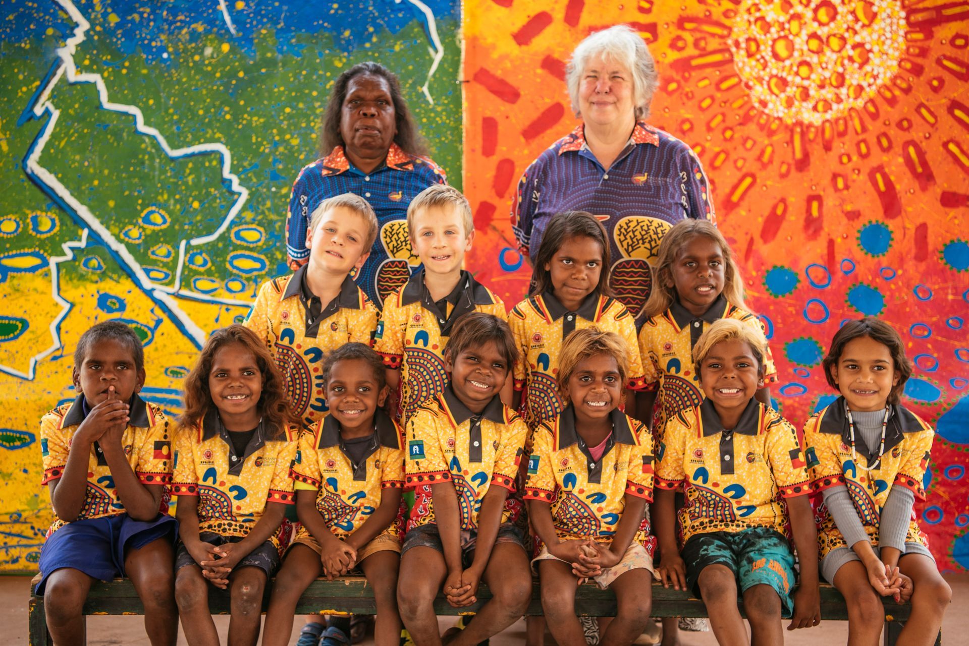 A group of children are posing for a picture in front of a colorful wall.
