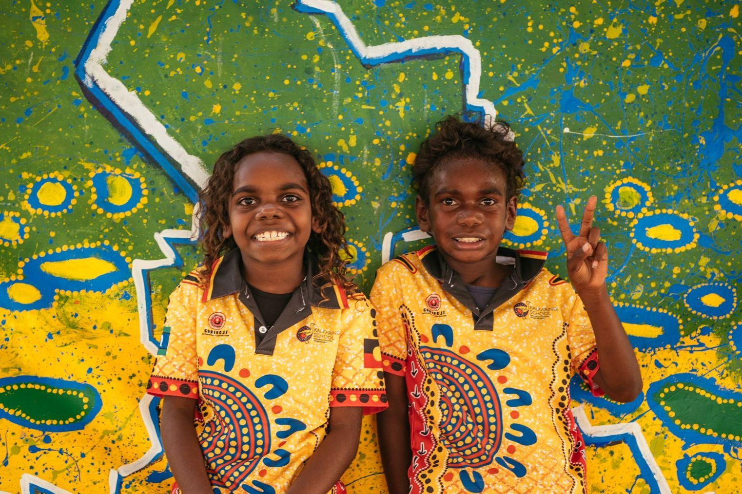 Two young girls are standing next to each other in front of a painting.