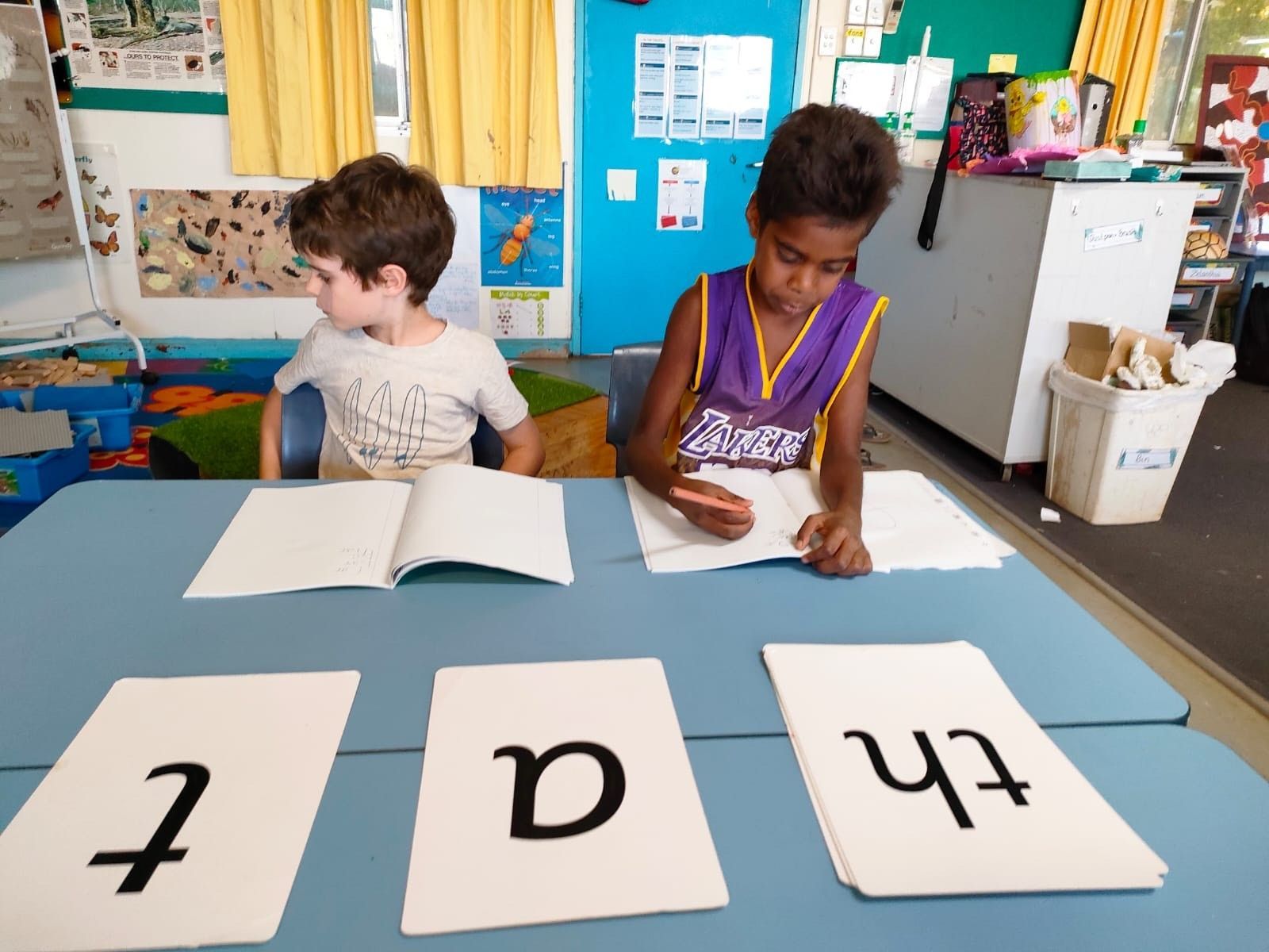 A boy wearing a lakers jersey sits at a table reading a book