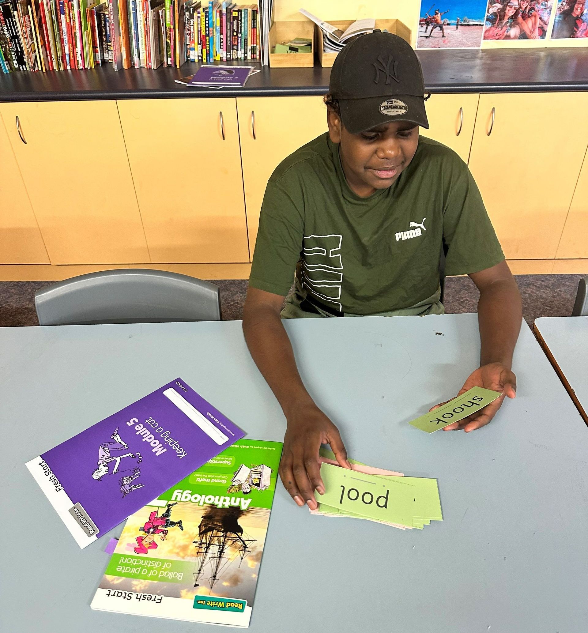 A boy is sitting at a table with books and a card that says puai