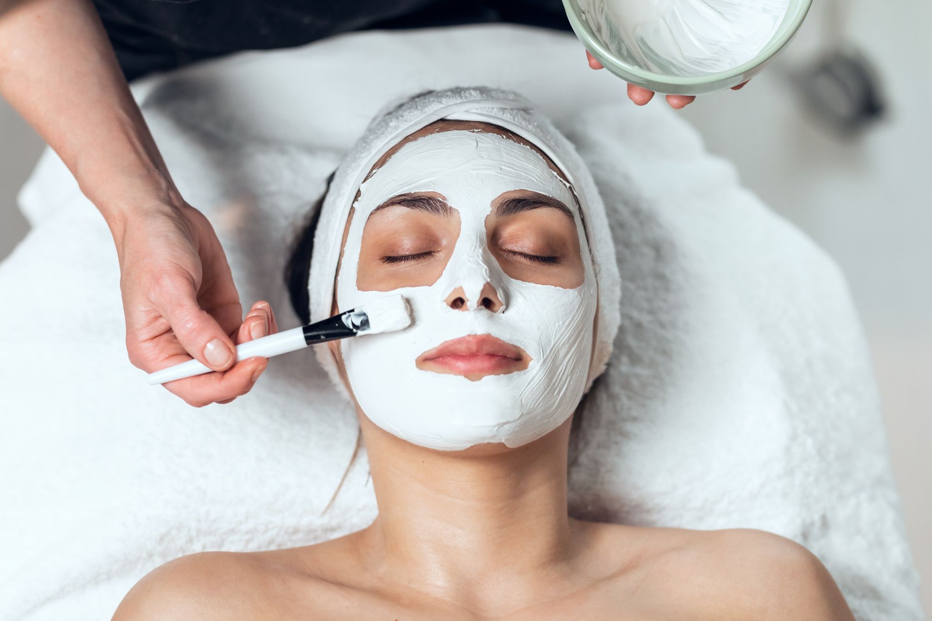 A woman is getting a white mask on her face at a spa.