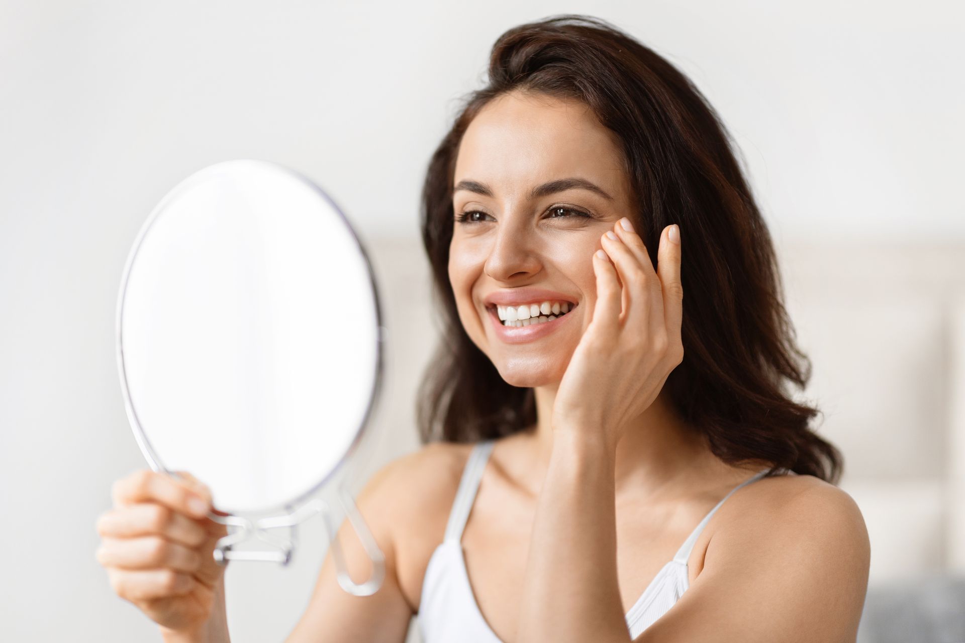 A woman is looking at her face in a mirror.