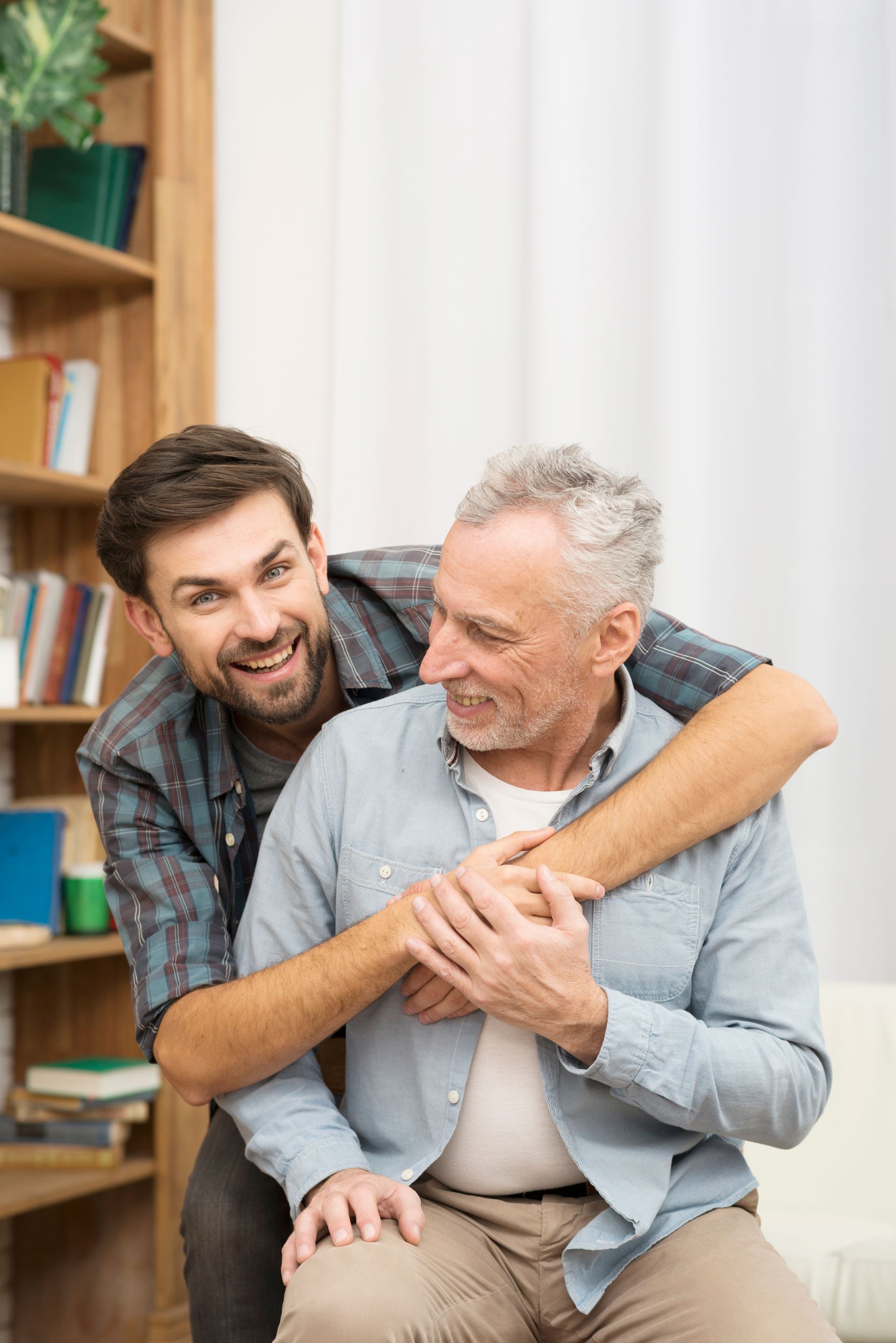 A young man is hugging an older man while sitting on a couch.