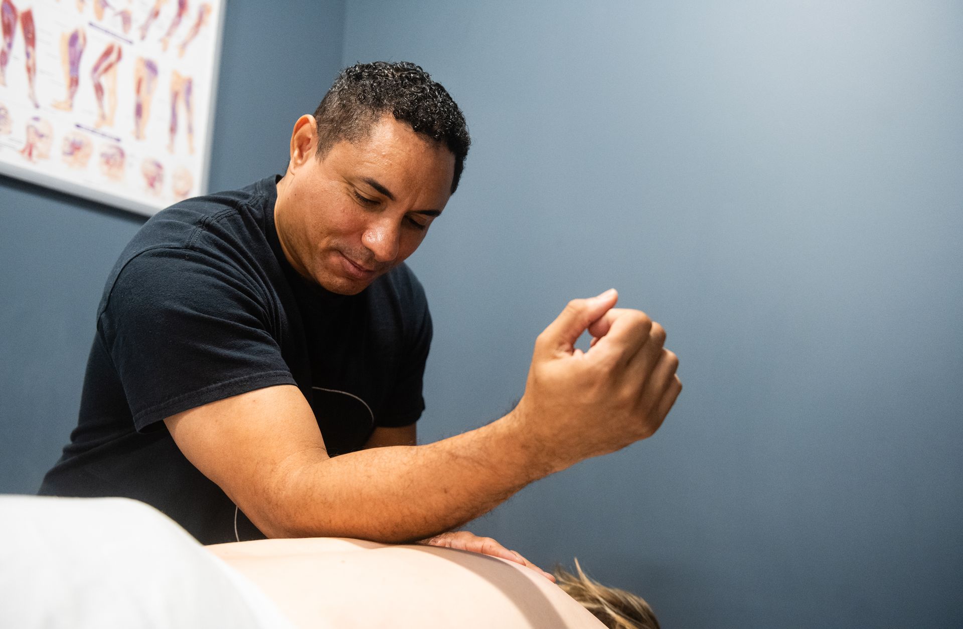 Massage therapist using elbow to apply pressure on a person's back; blue wall in the background.