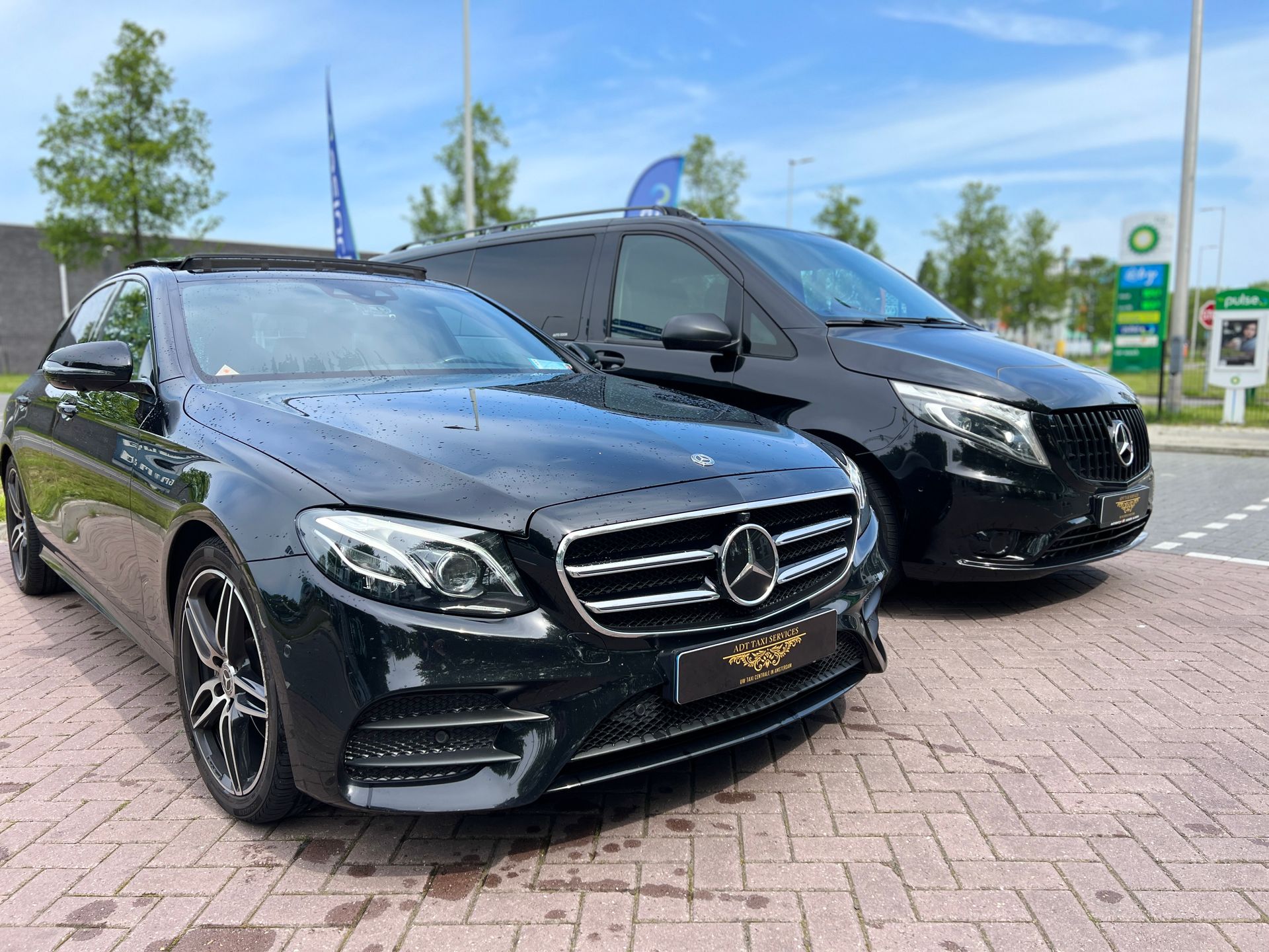 Twee zwarte auto's staan ​​naast elkaar geparkeerd op een stenen weg. Mercddes Chauffeur service amsterdam