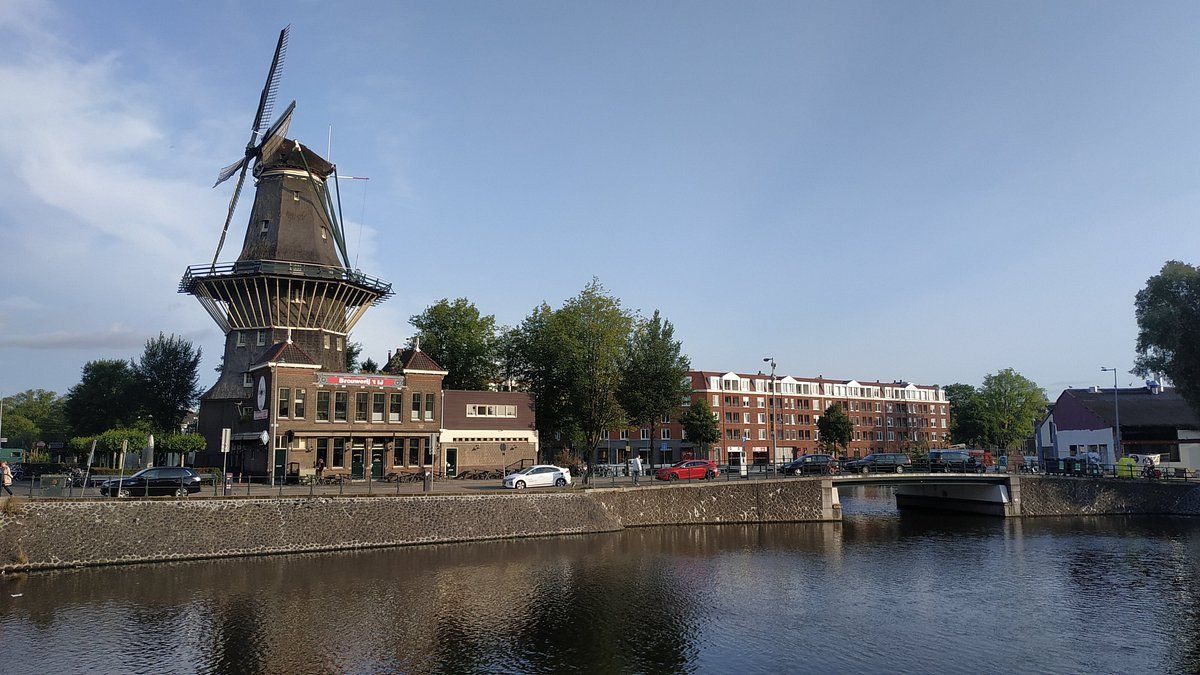 Een windmolen staat bovenop een gebouw naast een watermassa.