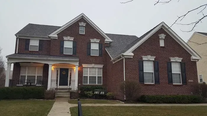 Brick house with dark blue shutters, gray roof, and porch. Gray sky.