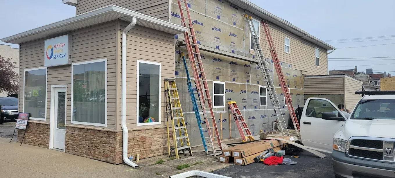 Building undergoing siding renovation, ladders propped against the exterior, work in progress.