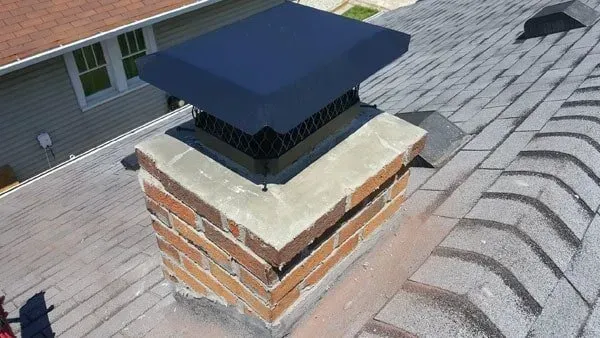 Brick chimney on a shingled roof with a black metal chimney cap.