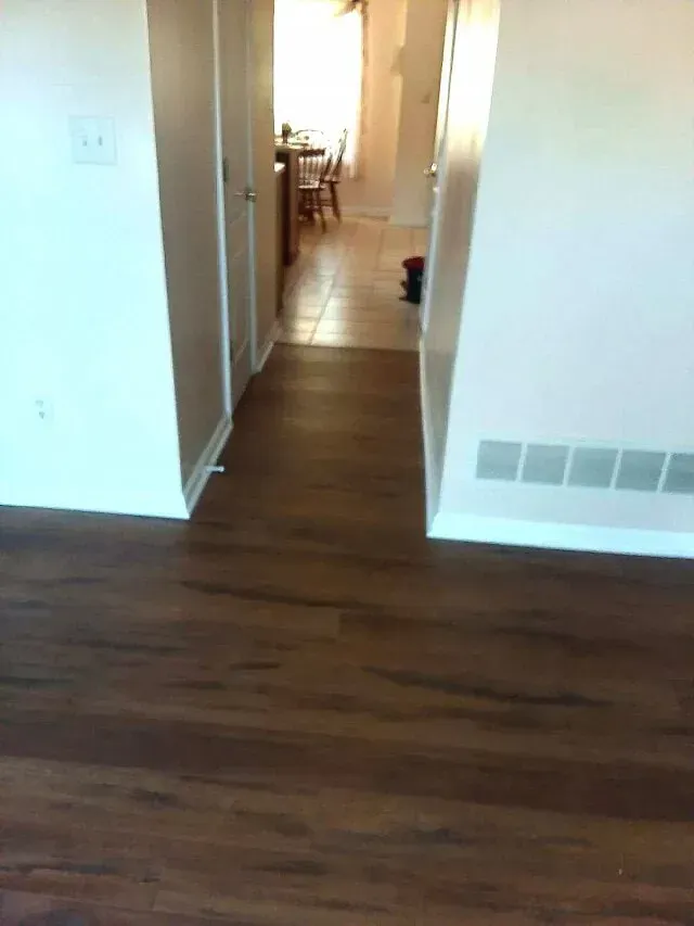 Hallway with dark wood-look flooring, light walls, two closed doors, and a glimpse into a kitchen.