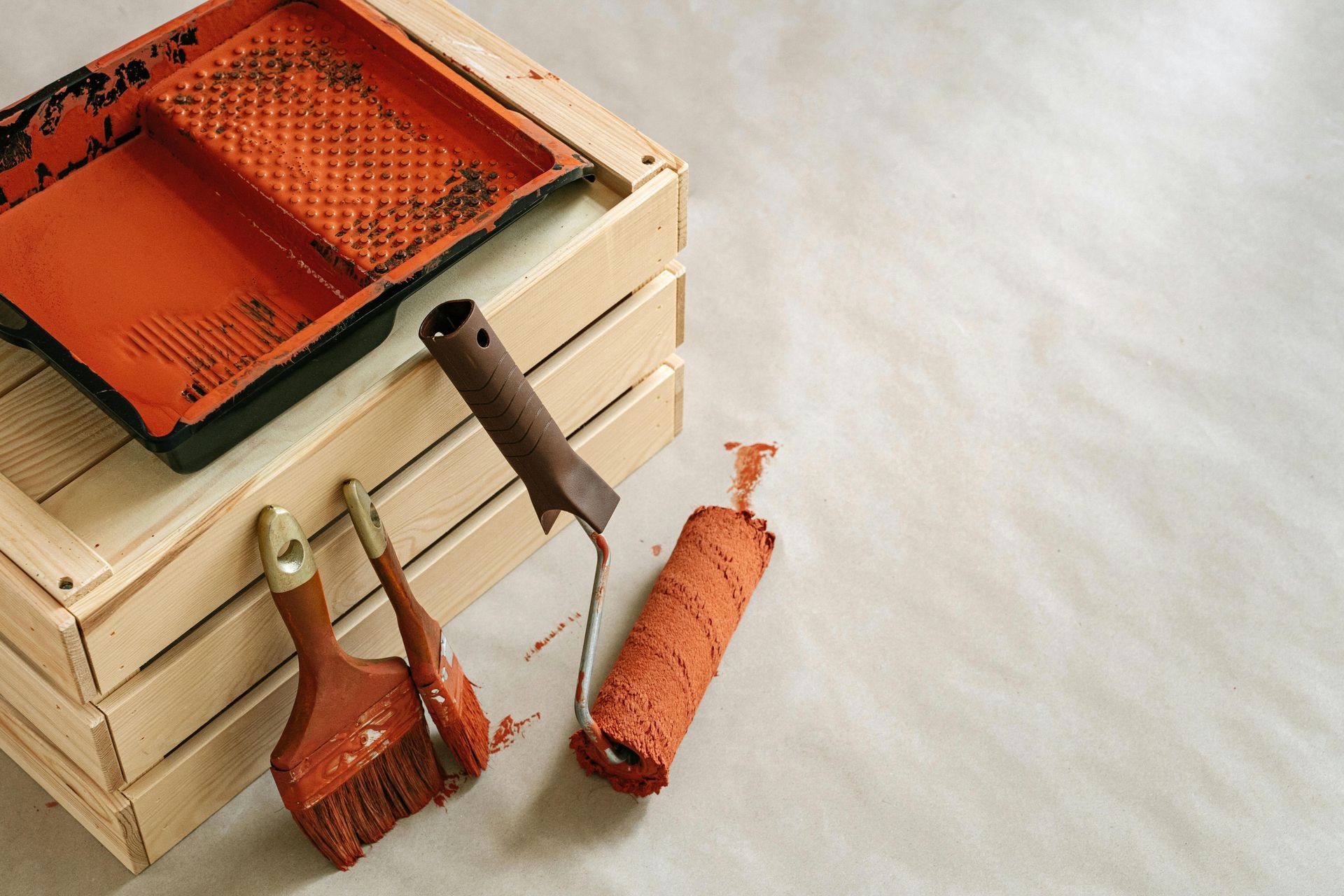 Paint supplies on a wooden crate: orange paint tray, brushes, and roller.
