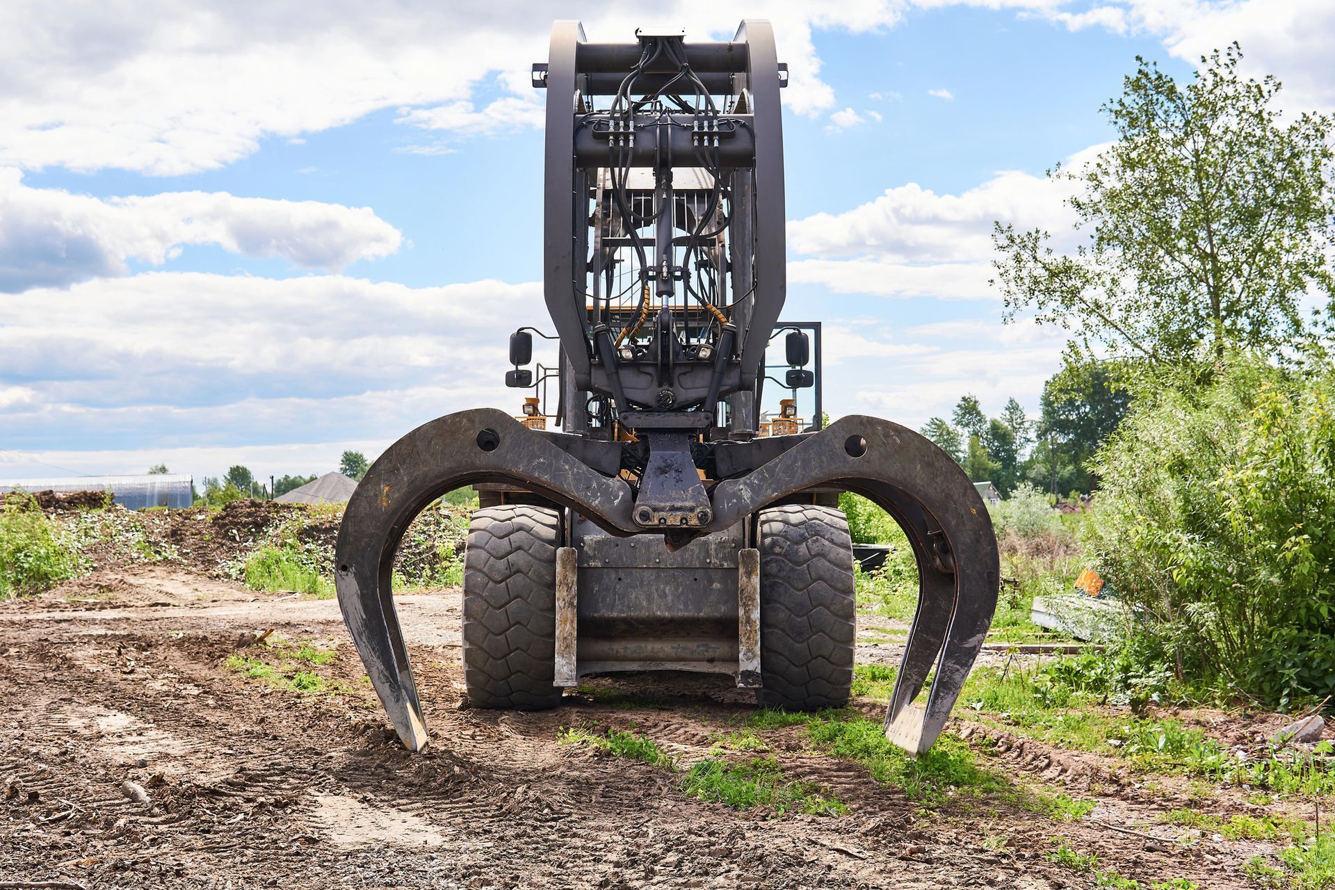 Large forestry machine with claw on muddy dirt path in a clearing, trees and blue sky in background