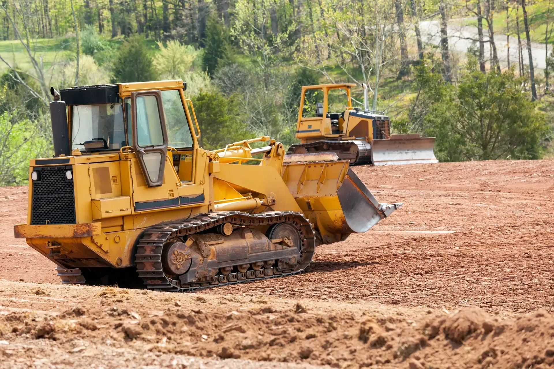 Two yellow bulldozers grading a dirt site with trees in the background