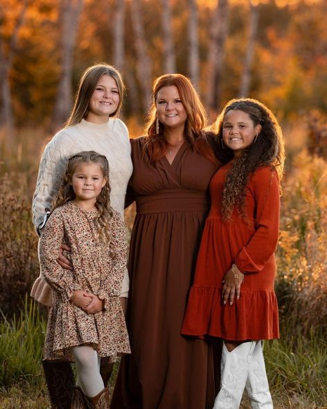 Four people standing together in a golden field at sunset, wearing earth-toned dresses and sweaters