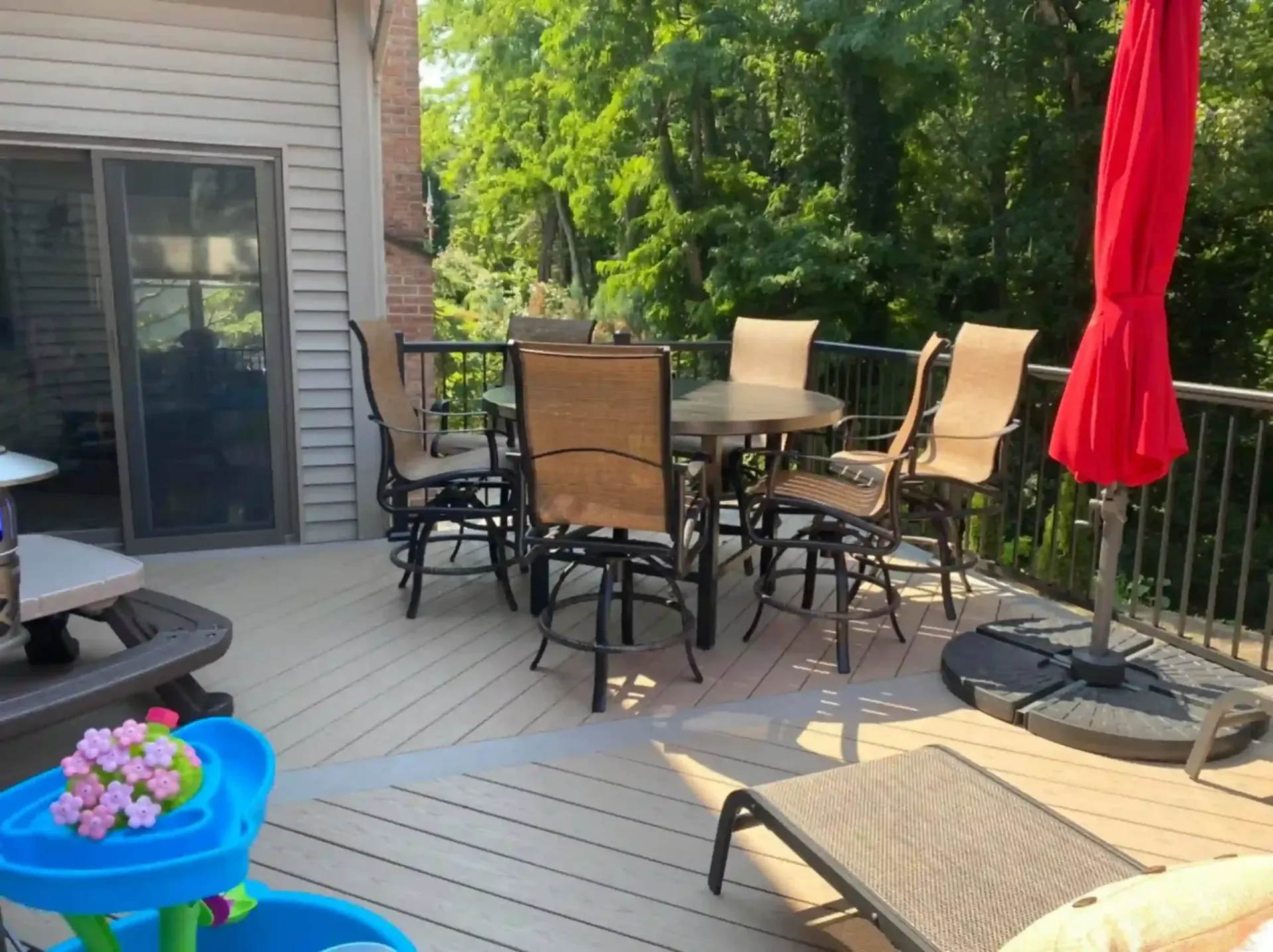 Deck with outdoor furniture, red umbrella, and view of trees.