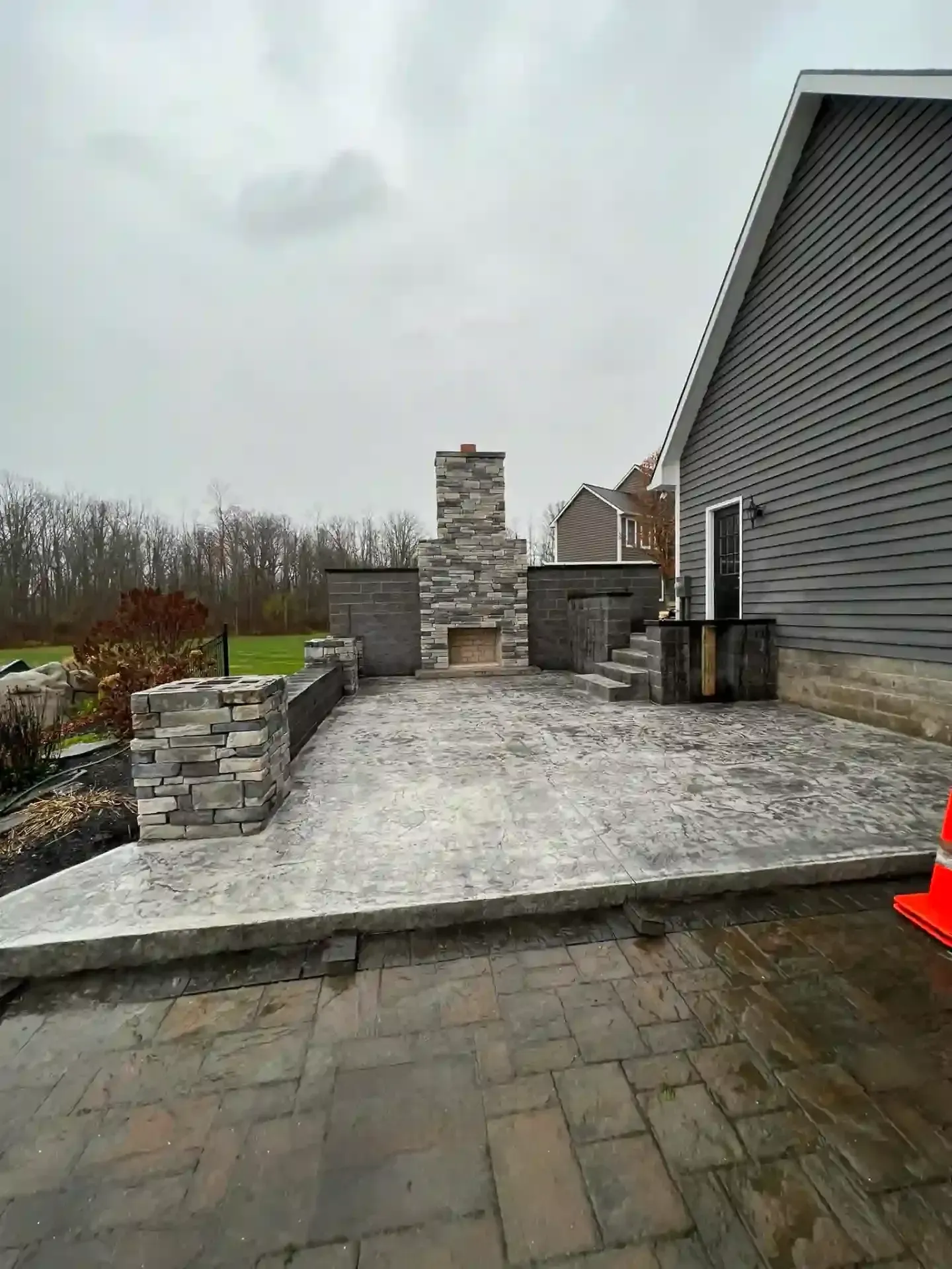 Outdoor patio with fireplace and stonework, gray pavers, overcast sky.