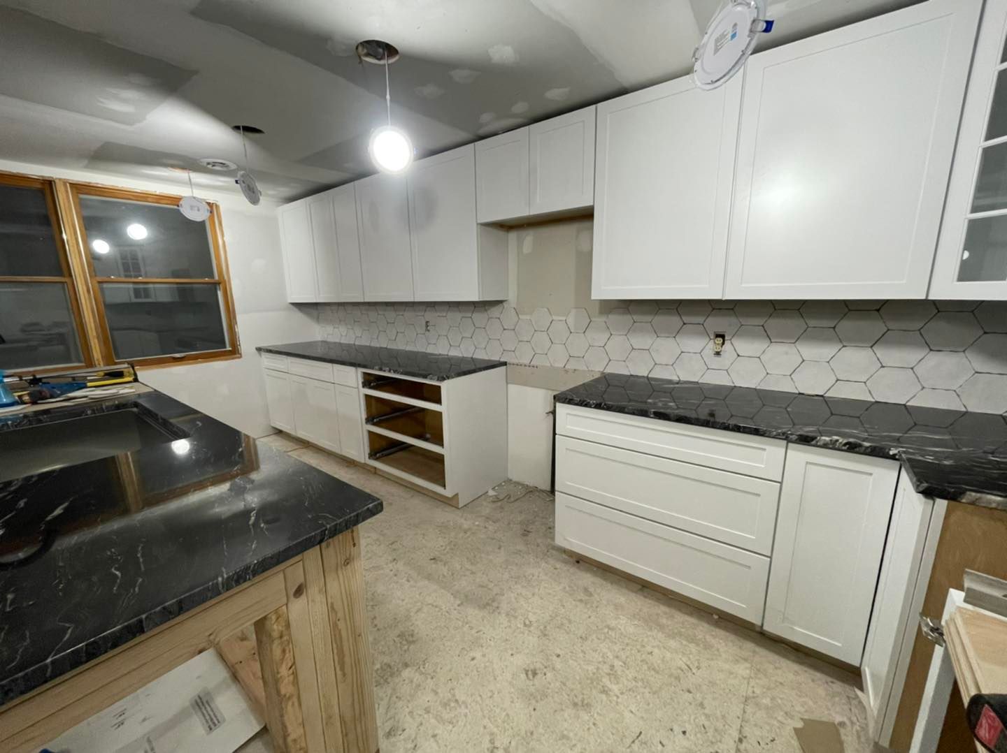 White kitchen cabinets with black countertops and hexagon tile backsplash under construction.