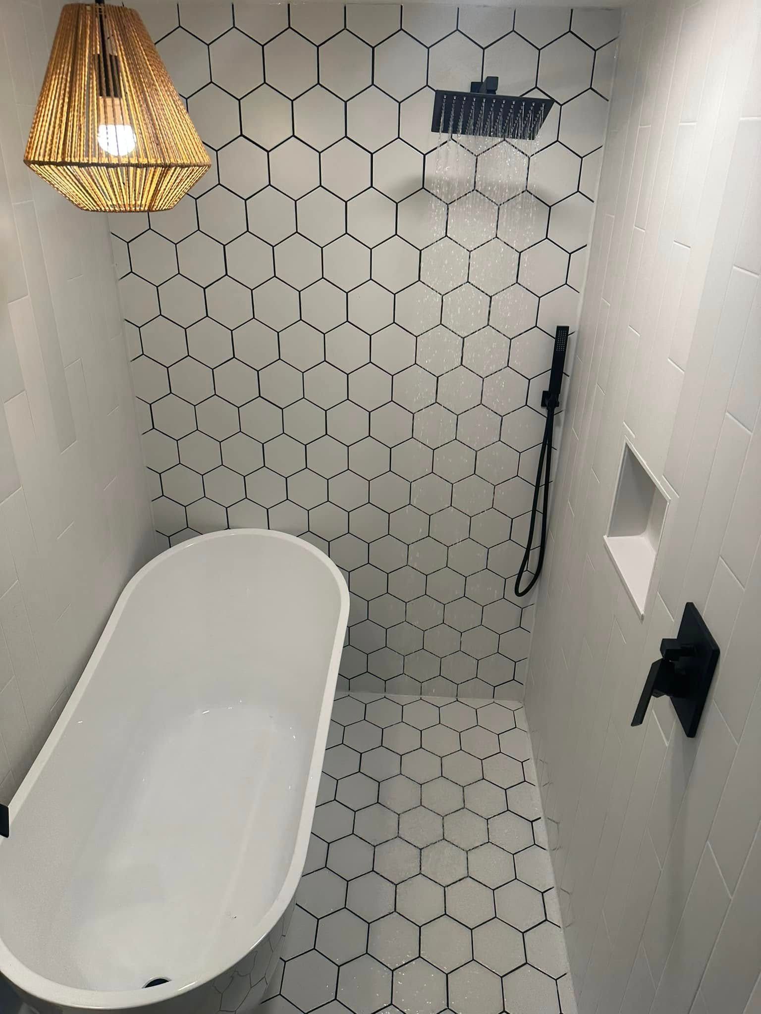 Bathroom with white hexagon tile, a freestanding tub, and black fixtures.