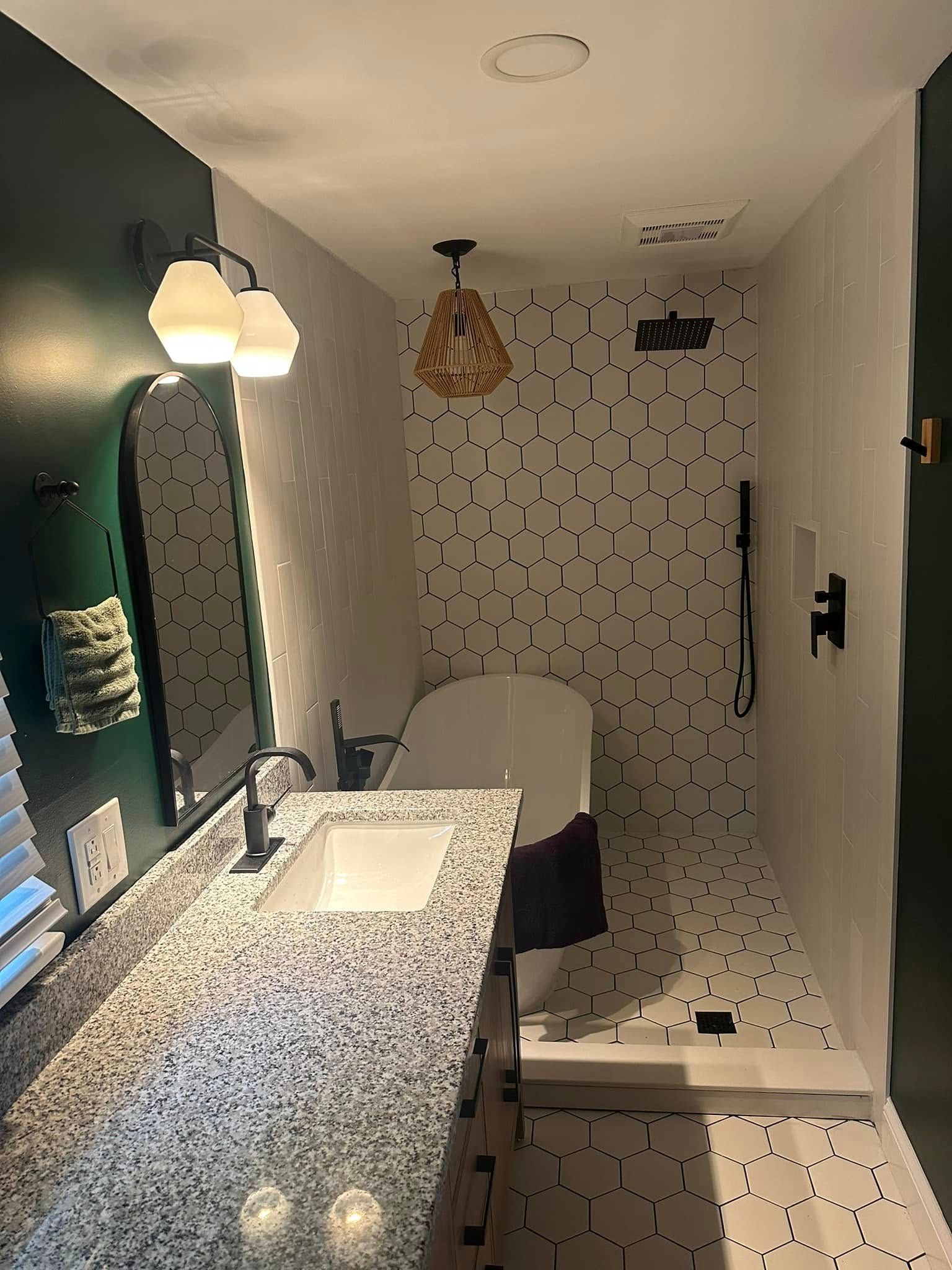 Modern bathroom with a patterned tile shower, freestanding tub, and dark green accent wall.