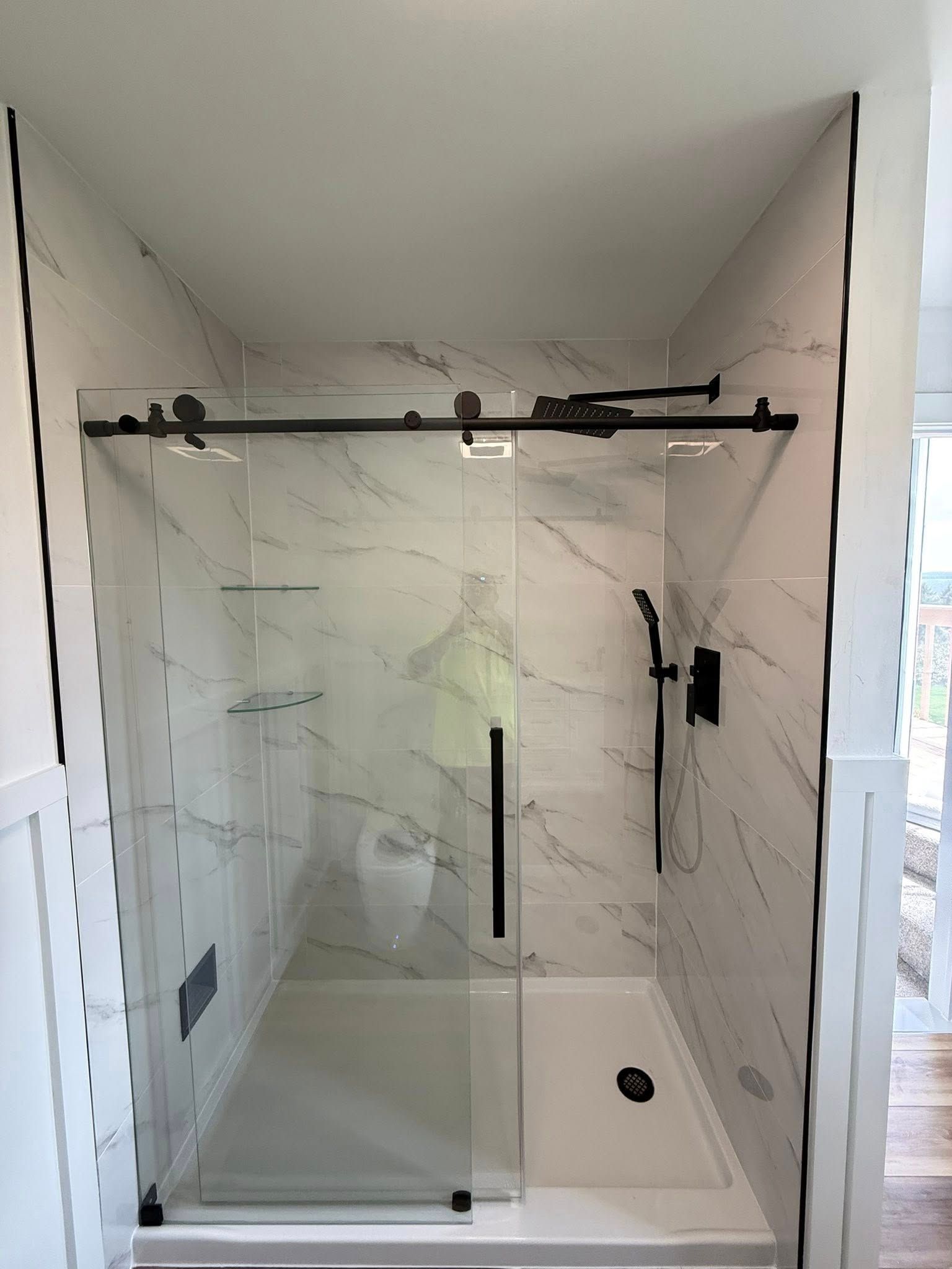 Modern glass shower enclosure with black hardware, marble-look tile, and a white shower pan.