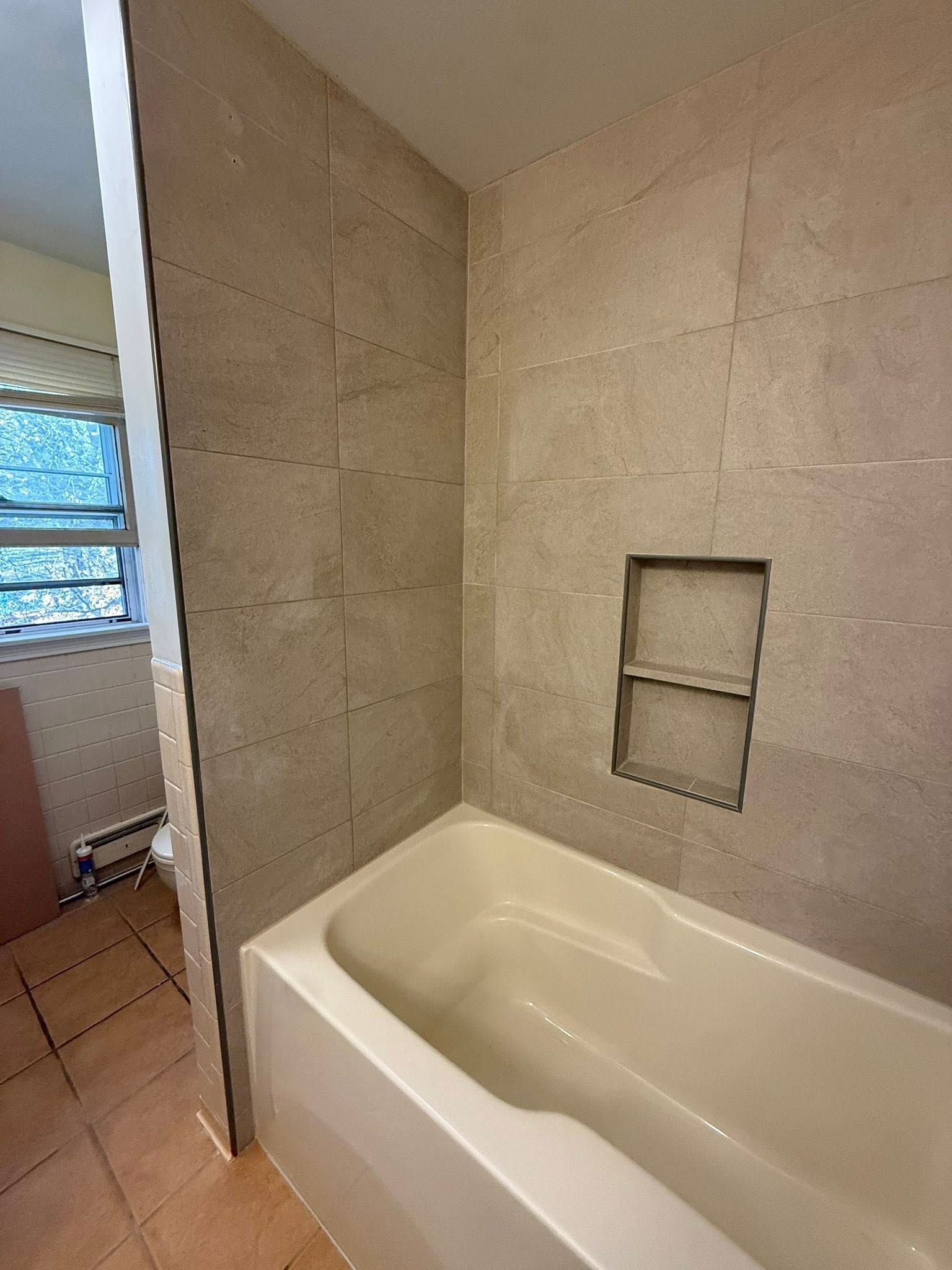 Bathtub with tiled walls and built-in shelf in a bathroom.
