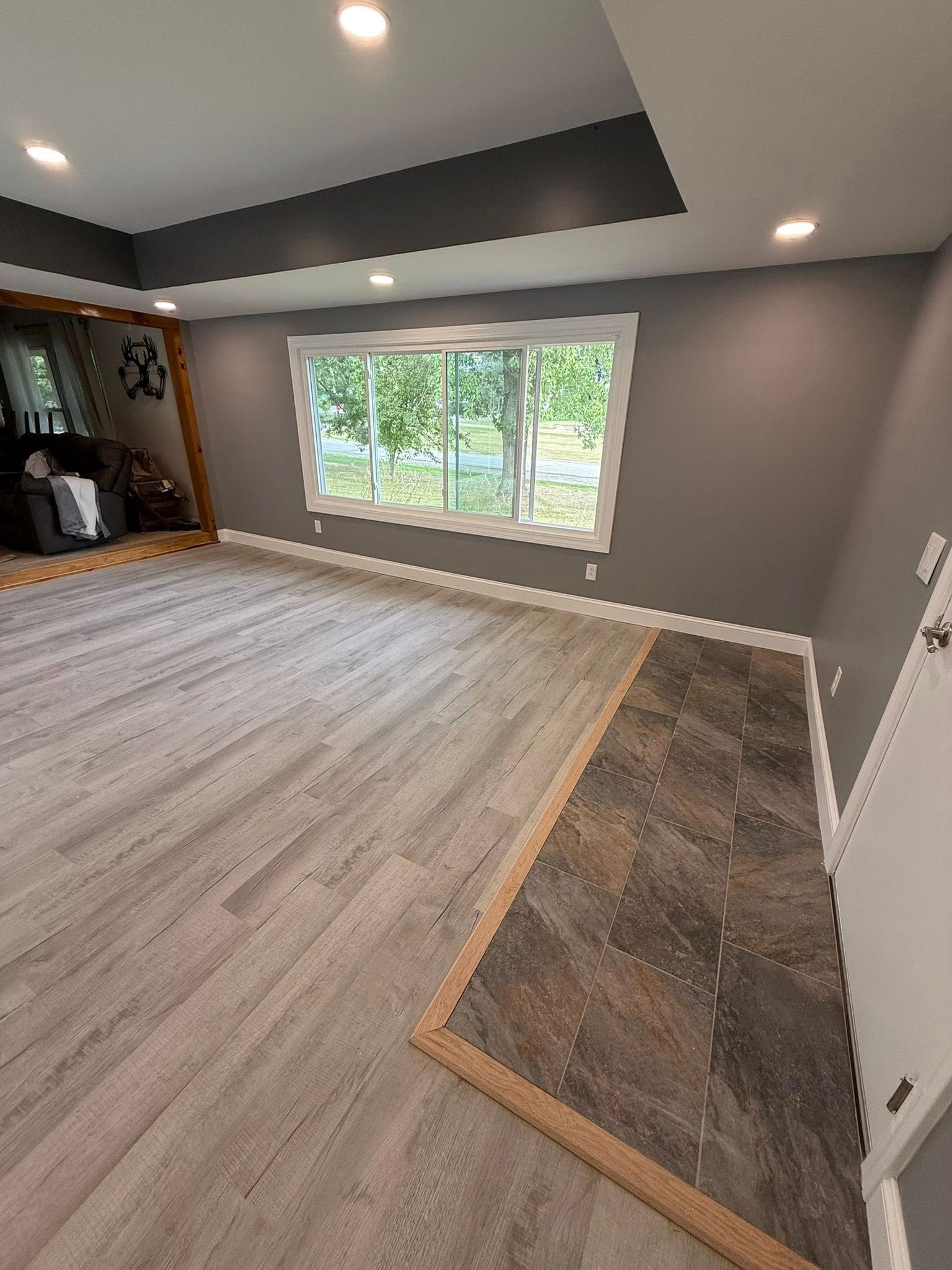 Living room with gray walls, light wood-look floors, and a dark tile section near a doorway.