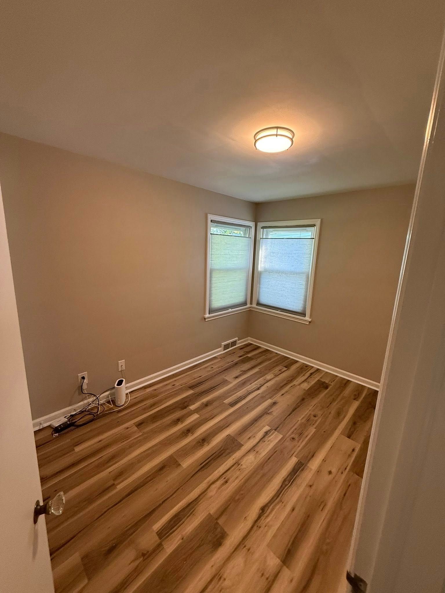 Empty room with wood-look flooring, tan walls, small windows, and a ceiling light.