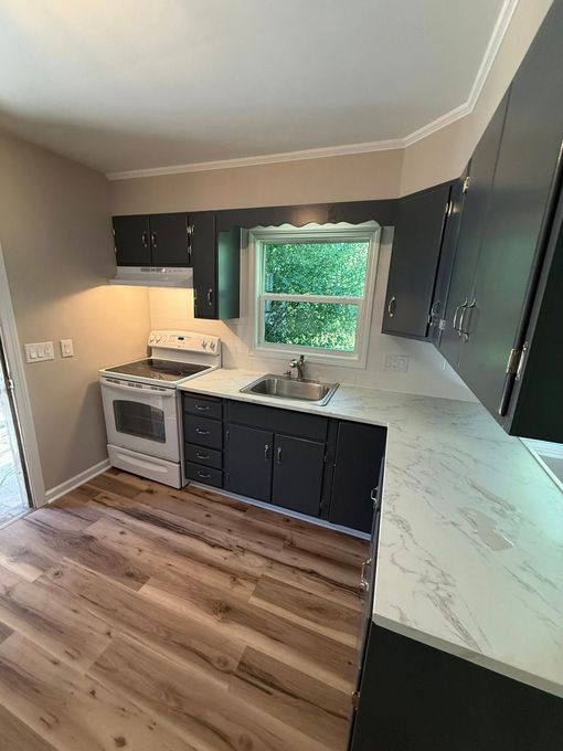 Kitchen under renovation; white cabinets, black countertops, hexagon tile backsplash, unfinished floor.