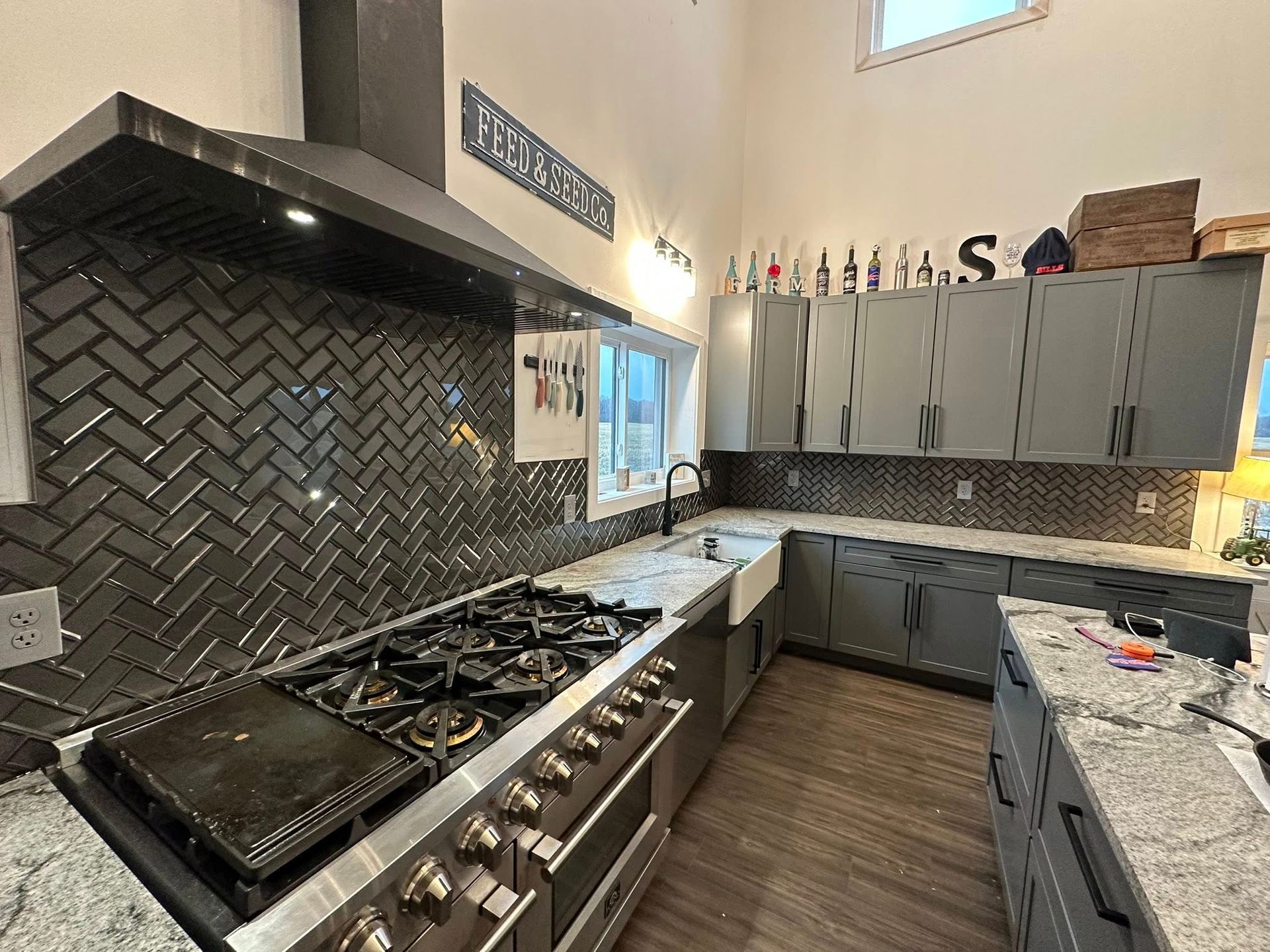 Modern kitchen with gray herringbone tile backsplash, stainless steel appliances, and gray cabinets.