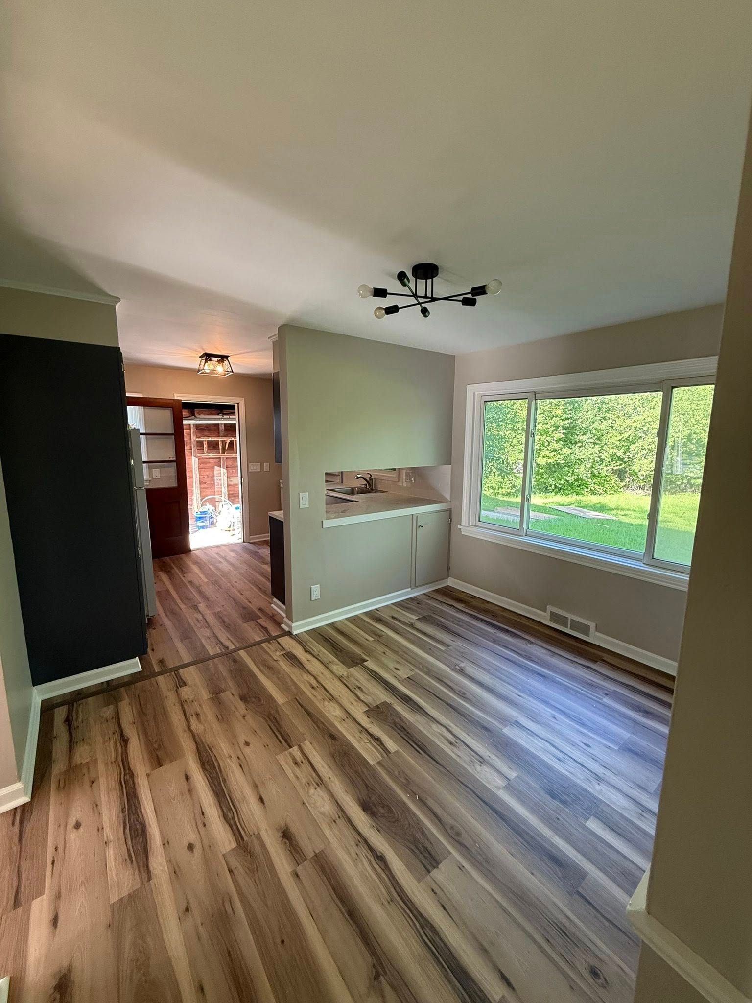 Interior view of a room with wood-look flooring, a window, and an entry to another space. Light gray walls.
