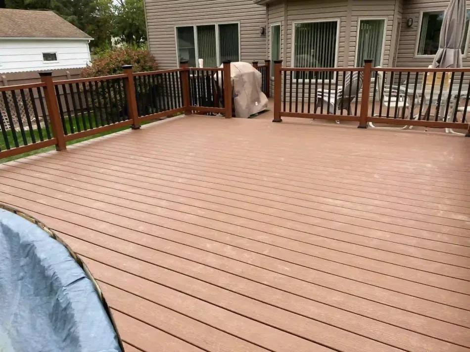Brown composite deck with railing, connected to a house with large windows.