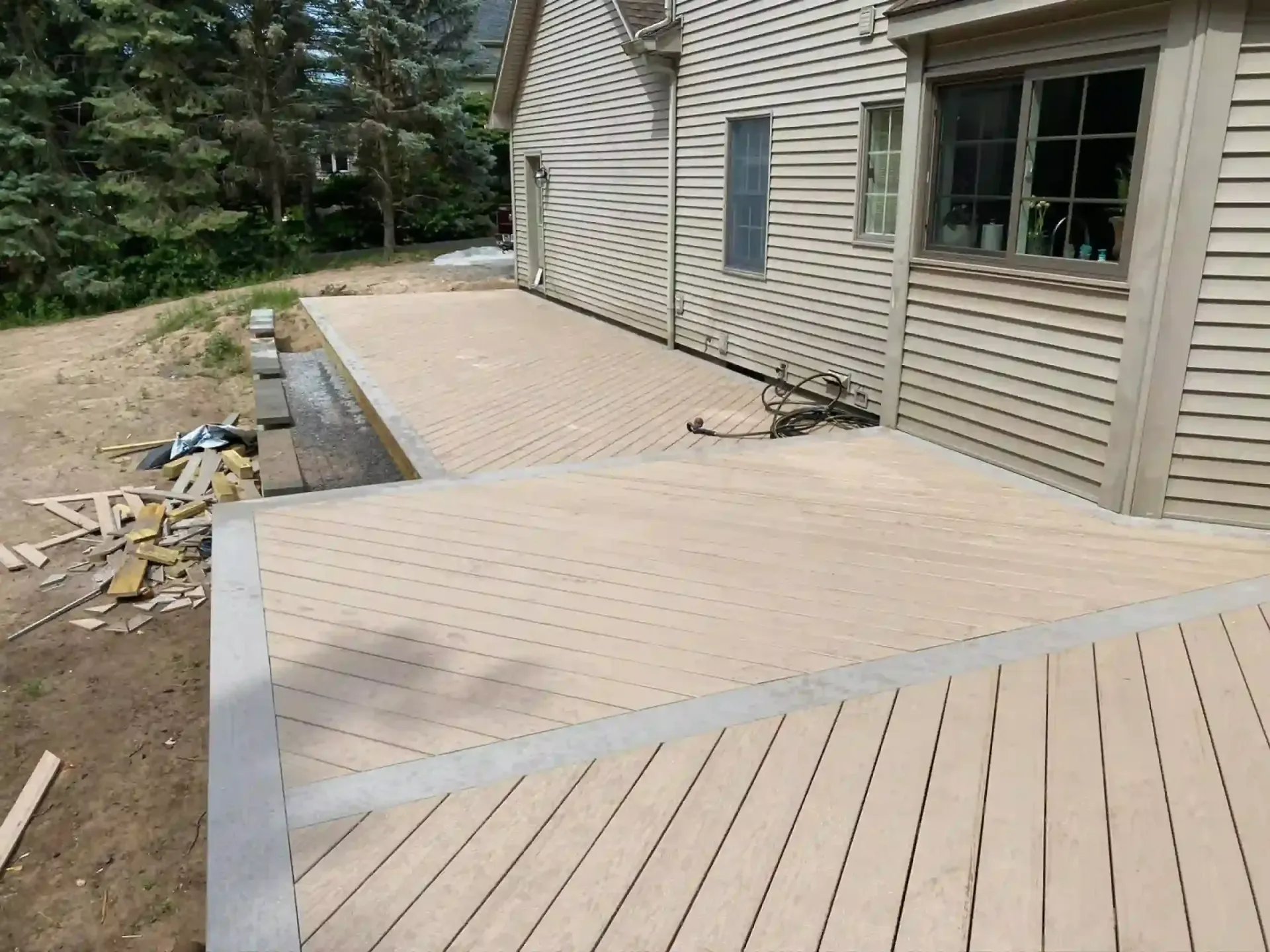 Composite deck next to a house with beige siding. Gray trim on deck edges, some construction debris.