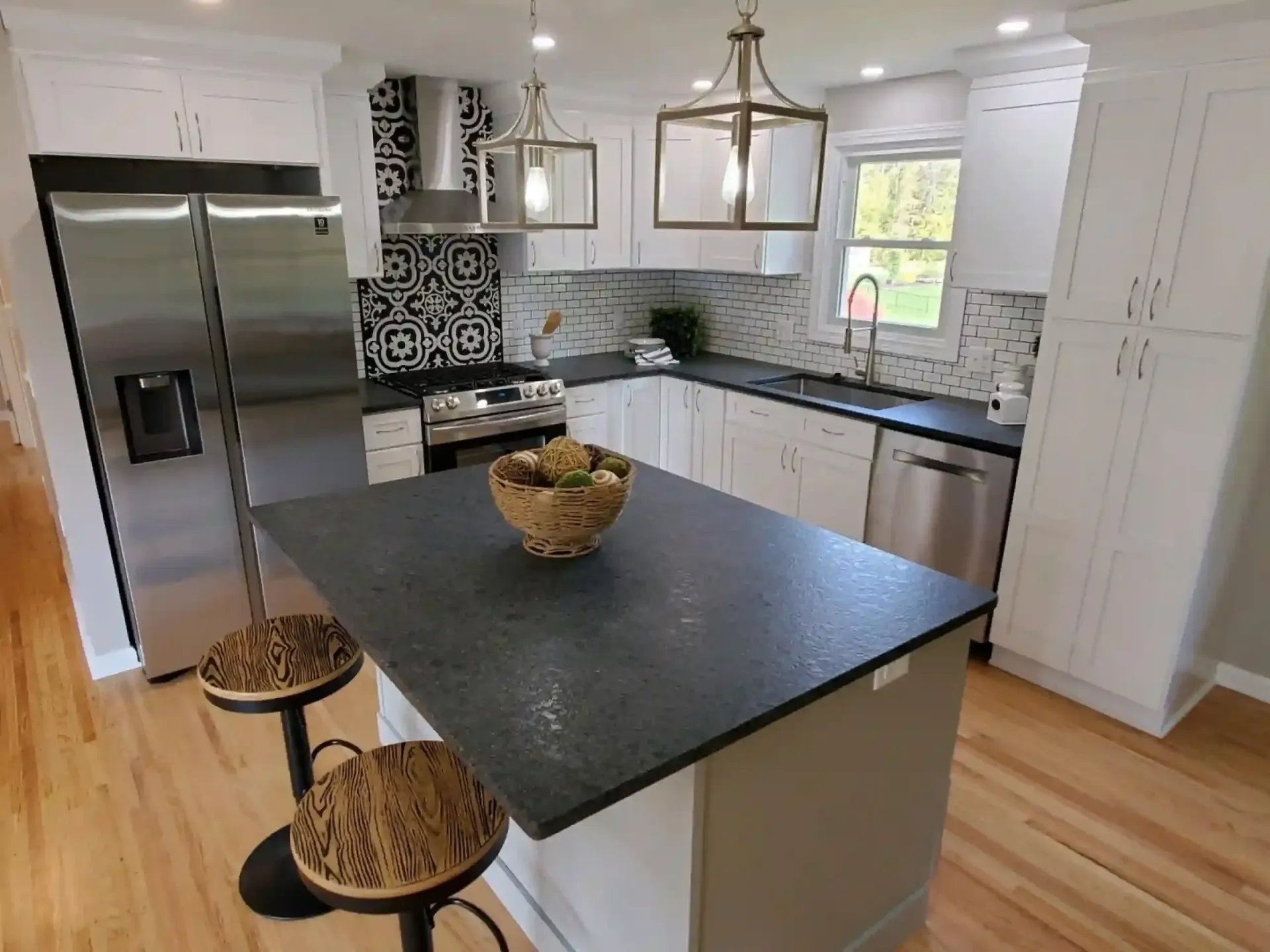 Modern kitchen with white cabinets, dark countertops, island with stools, and stainless steel appliances.