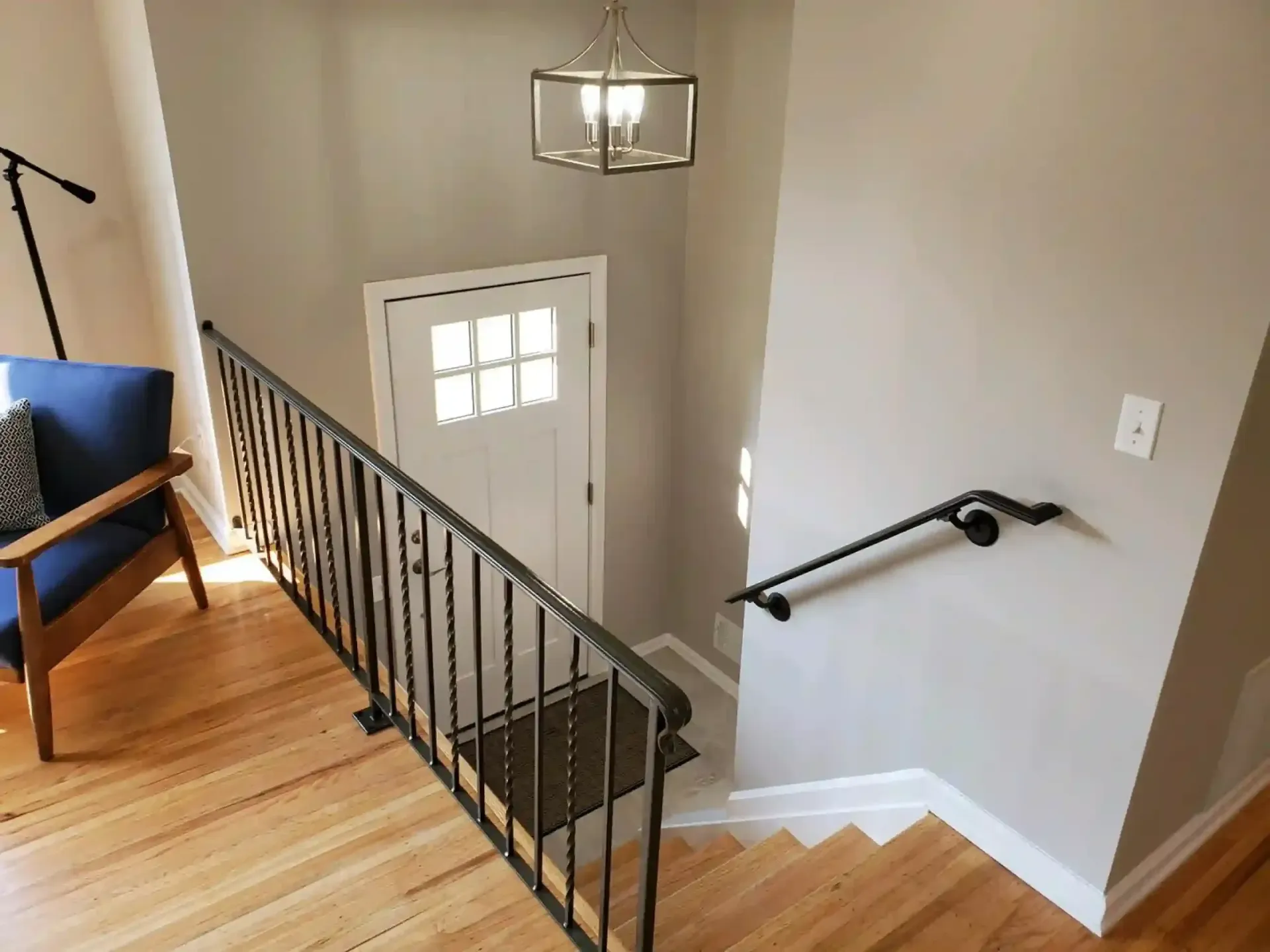 Staircase leading down to a white door, black railing, wooden floors. Blue armchair in the corner.