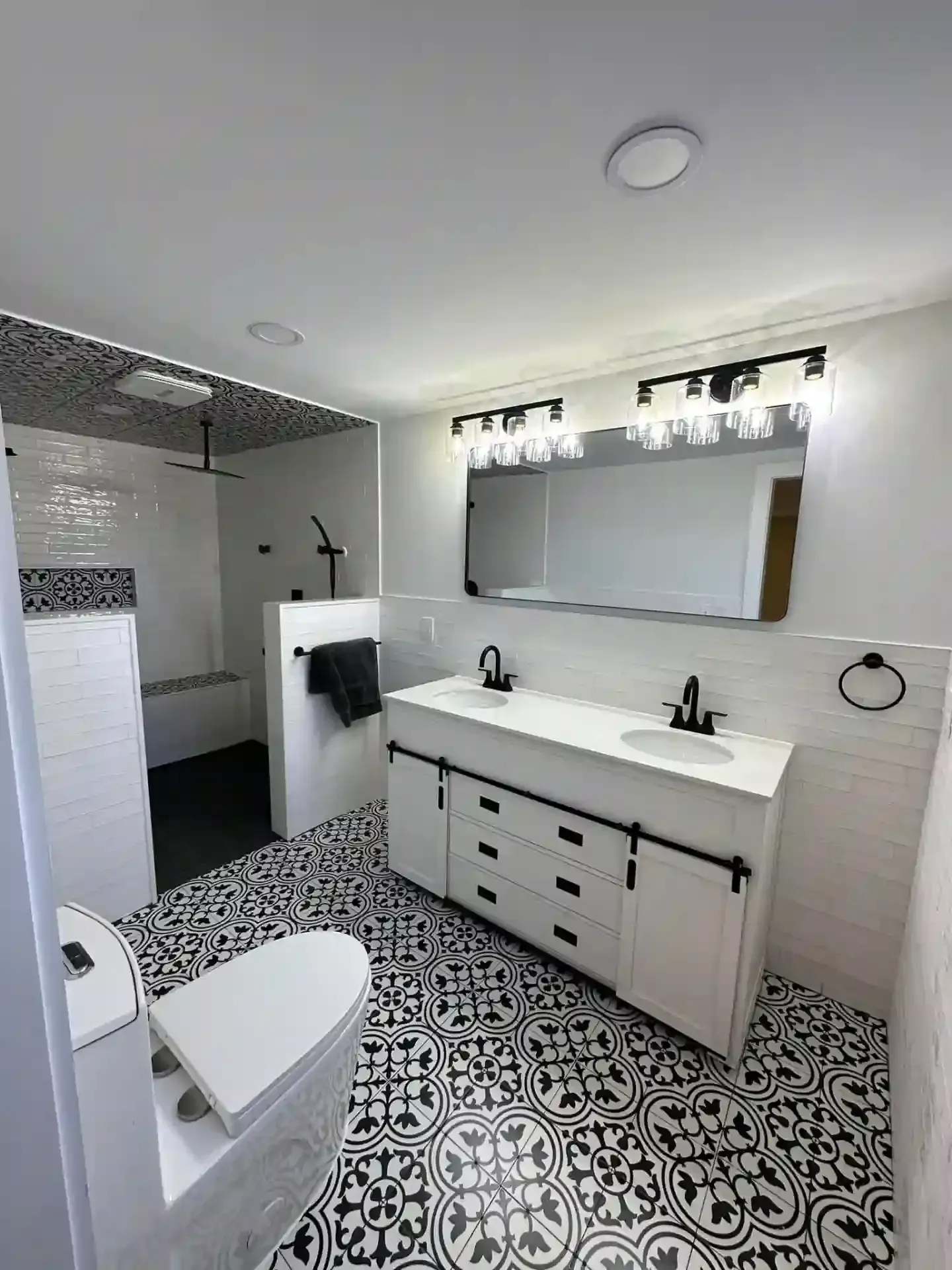 Modern bathroom with black and white patterned tile floor, white vanity with black fixtures, and a large mirror.