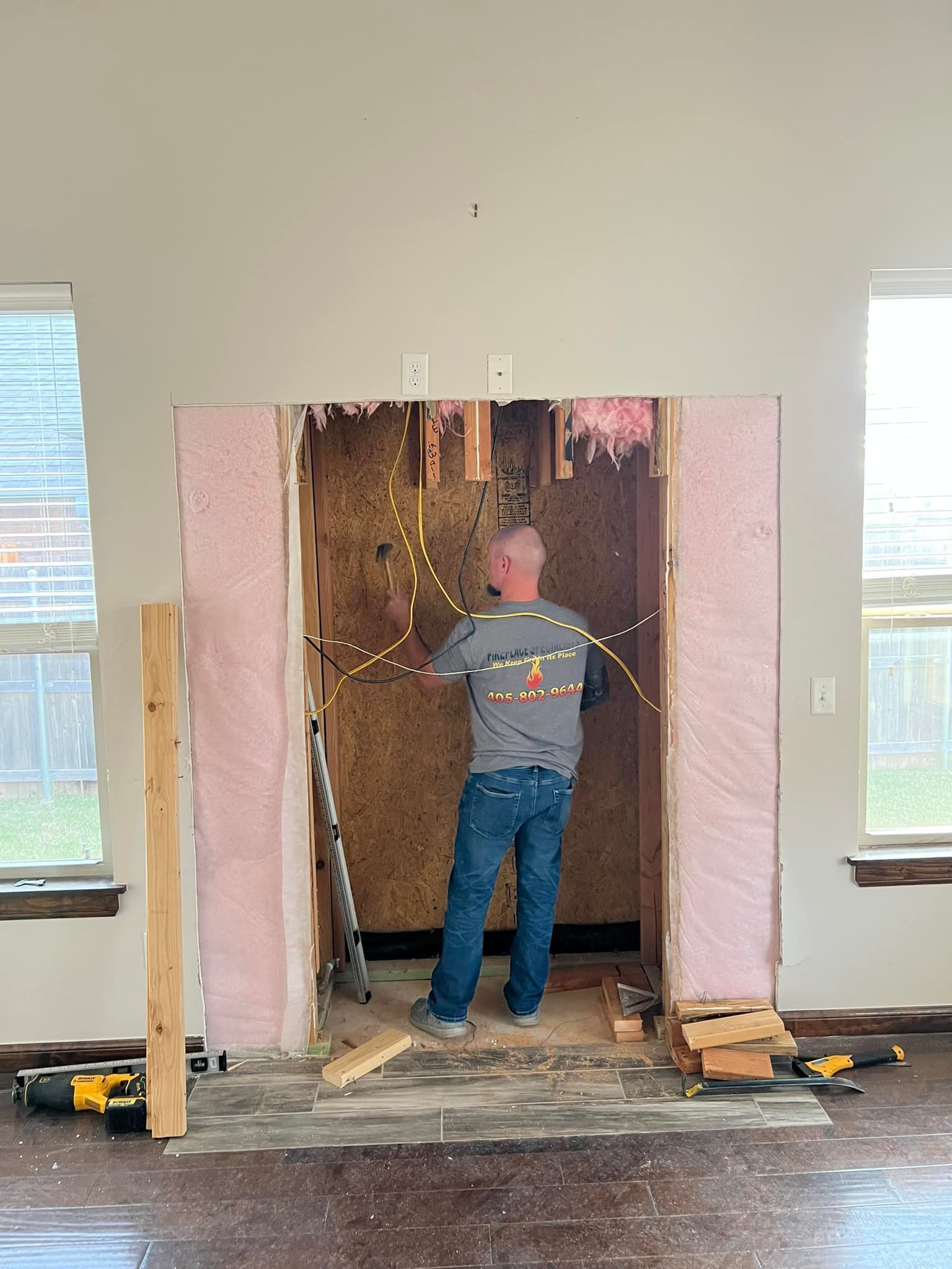 A person working on electrical wiring inside a wall. Pink insulation and construction tools are visible. A person working on electrical wiring inside a wall. Pink insulation and construction tools are visible.