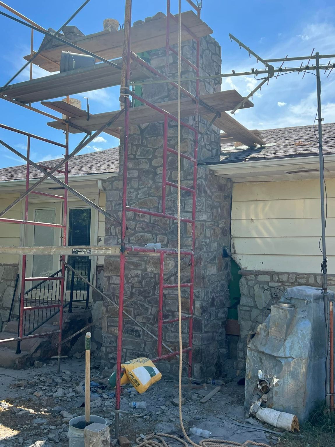 Chimney under construction, surrounded by scaffolding. The chimney is made of stone and is attached to a house.