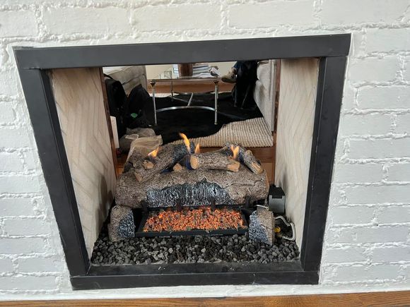 Electric fireplace in a brick-surrounded inset, black trim, with artificial flames and glowing embers.