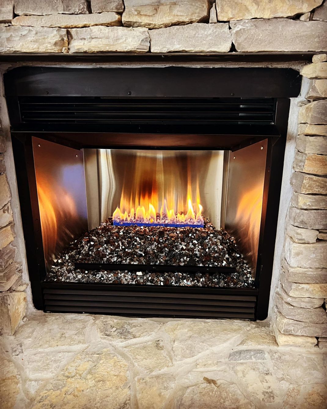Fireplace with flames and black glass stones, set in a stone surround, black metal trim.