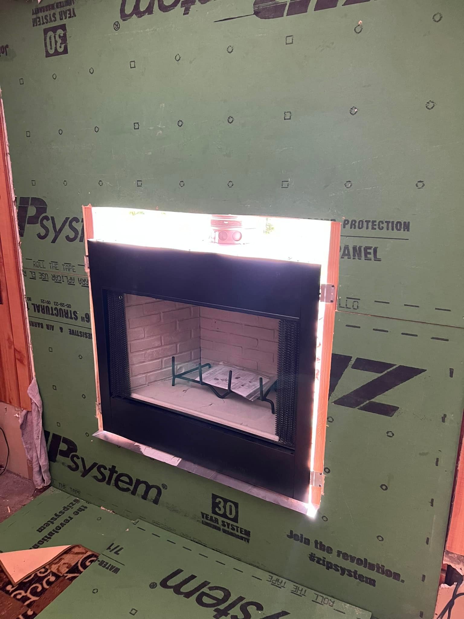 A black fireplace insert installed in a wall opening, surrounded by green sheathing. A black fireplace insert installed in a wall opening, surrounded by green sheathing.