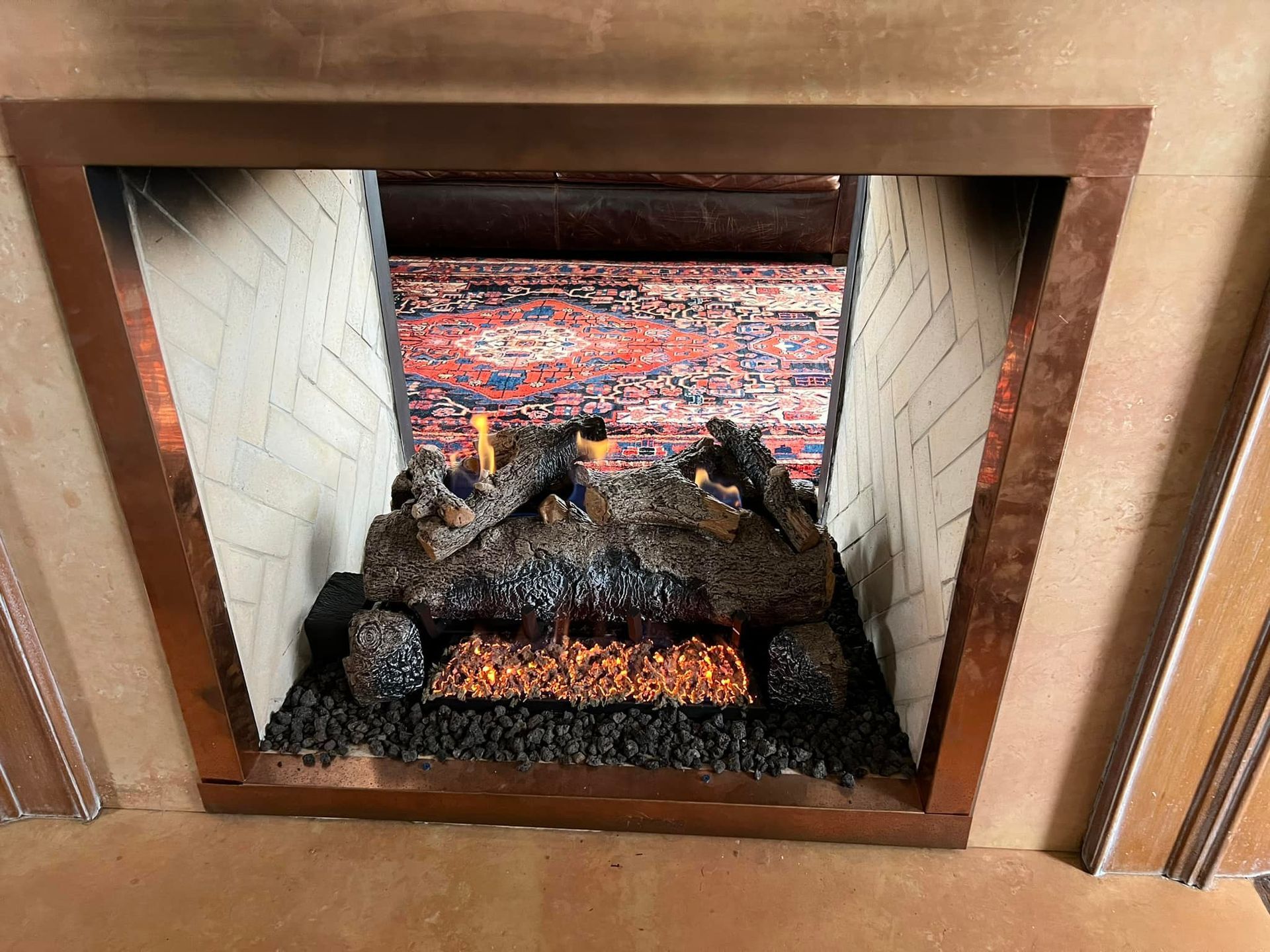 Fireplace with copper trim, faux logs, and a patterned rug in the back. Fireplace with copper trim, faux logs, and a patterned rug in the back.