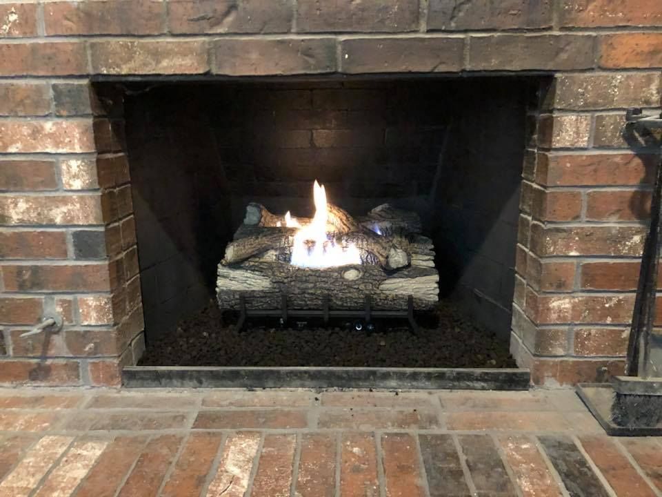 A brick fireplace with gas logs burning, set inside a brick surround.