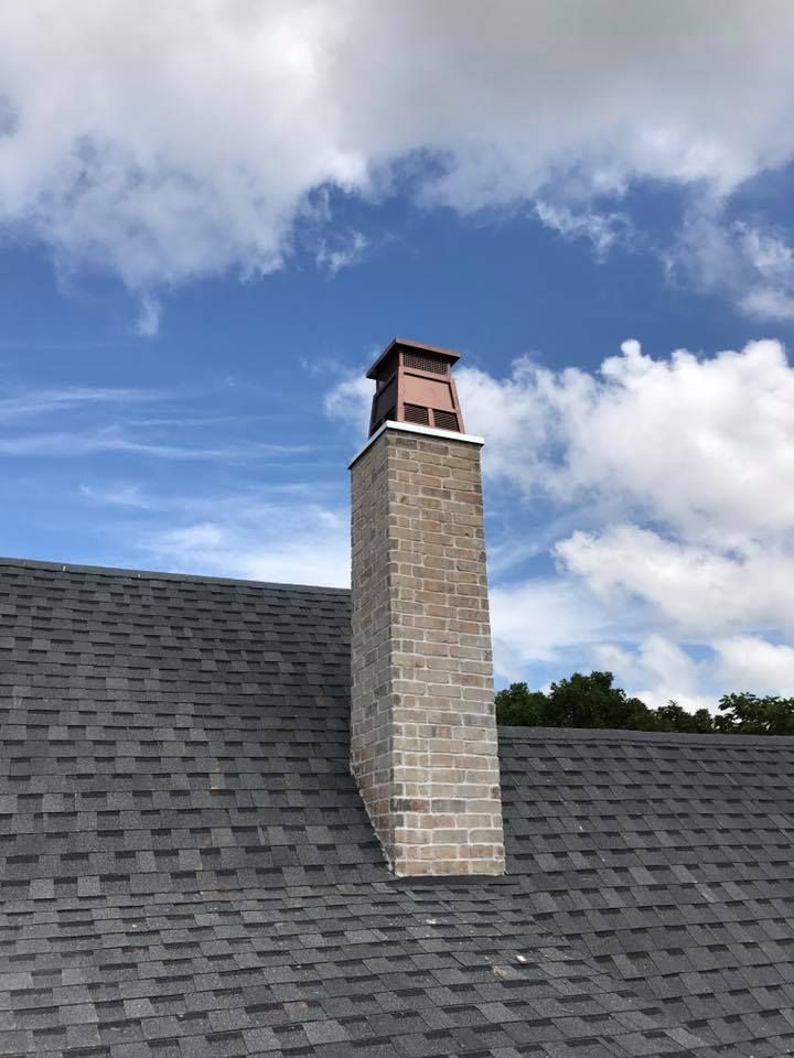 Brick chimney on a dark shingled roof against a blue sky with clouds. Brick chimney on a dark shingled roof against a blue sky with clouds.