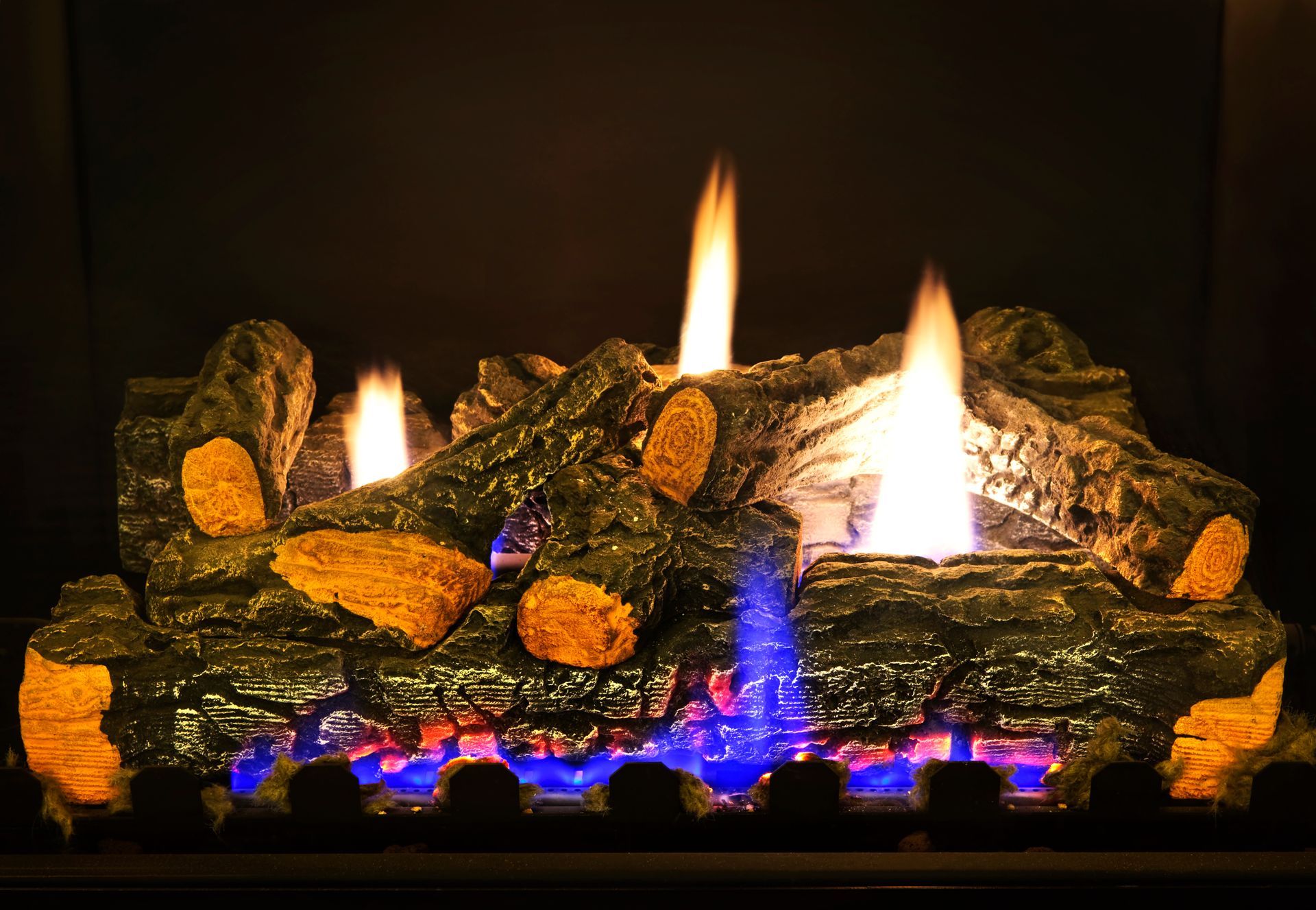 Gas log set burning with blue flames and glowing embers inside a fireplace.