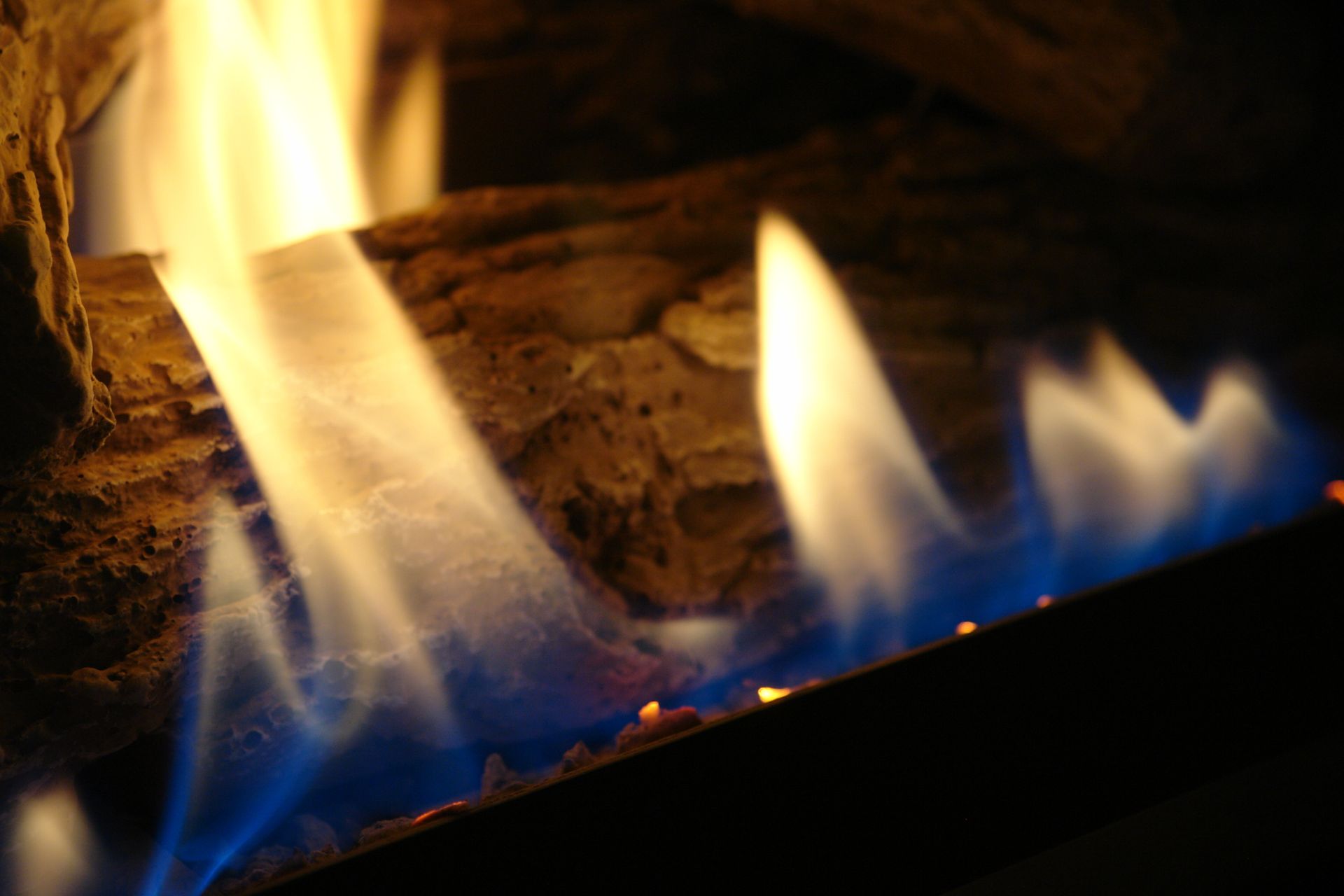 Close-up of blue and yellow flames burning beneath ceramic logs in a gas fireplace.
